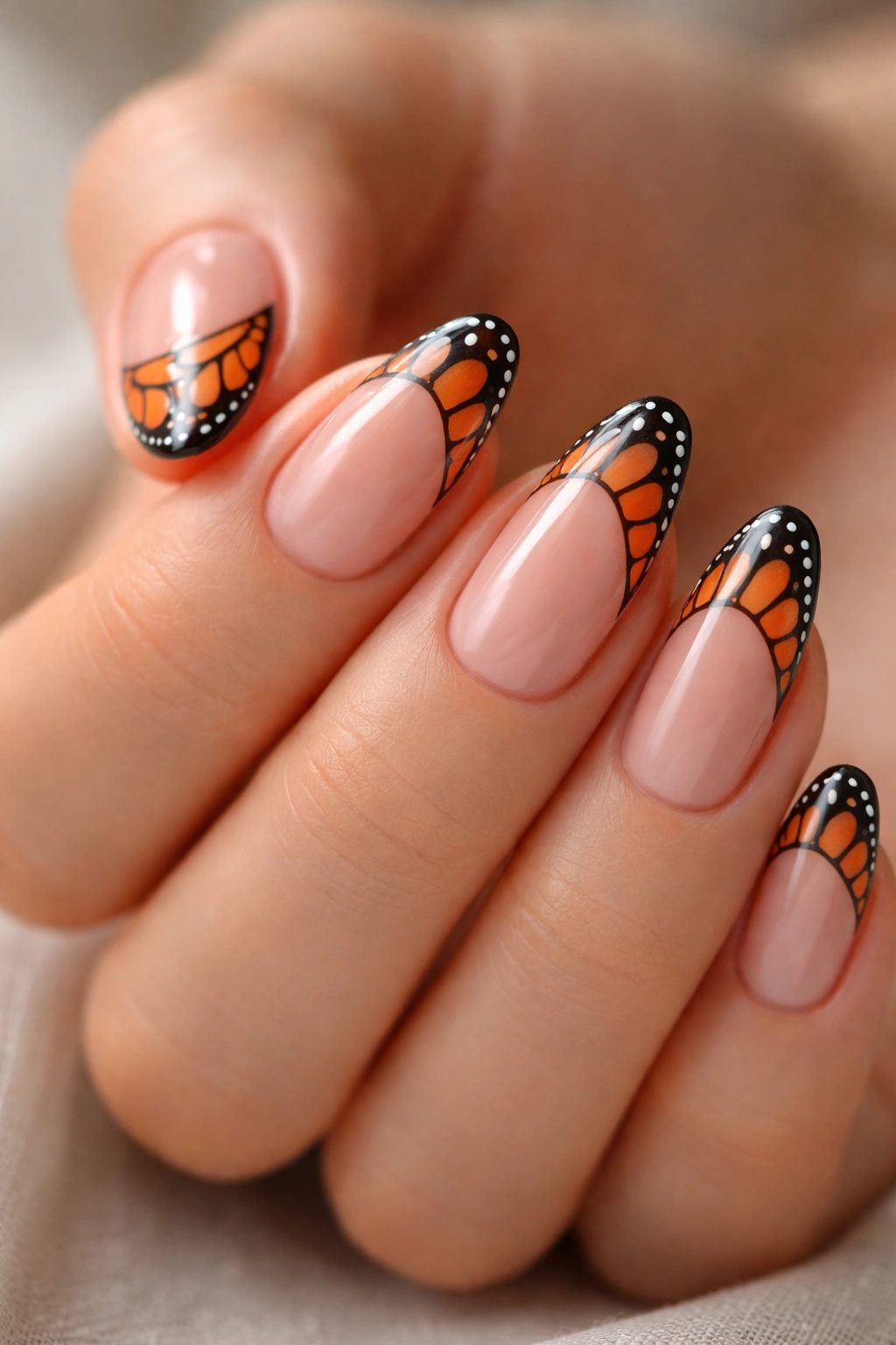 Short almond nails with peach blush base and monarch wing tips featuring black veins and white dots