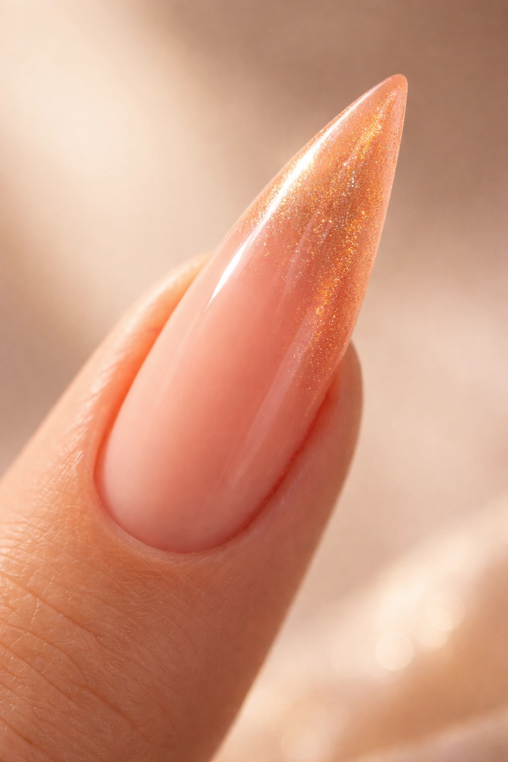 Soft peach curved stiletto nail with peach-to-gold shimmer along the tip