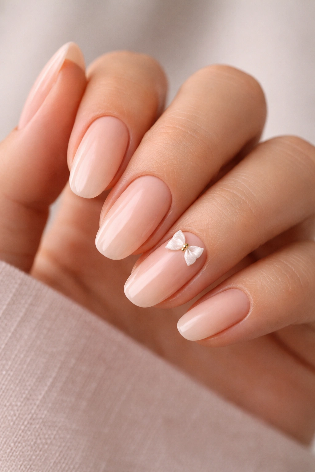 Close-up of peach ballerina nails with a small flat-backed 3D bow on one nail