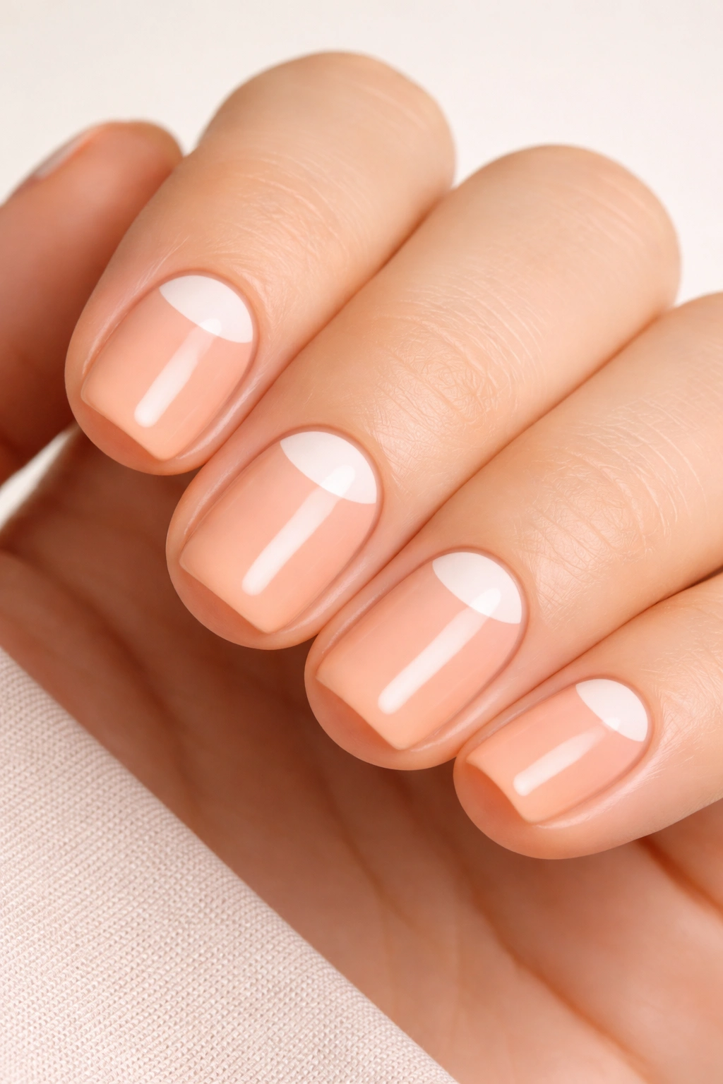 Close-up of short squoval nails in soft peach with white half-moon at base