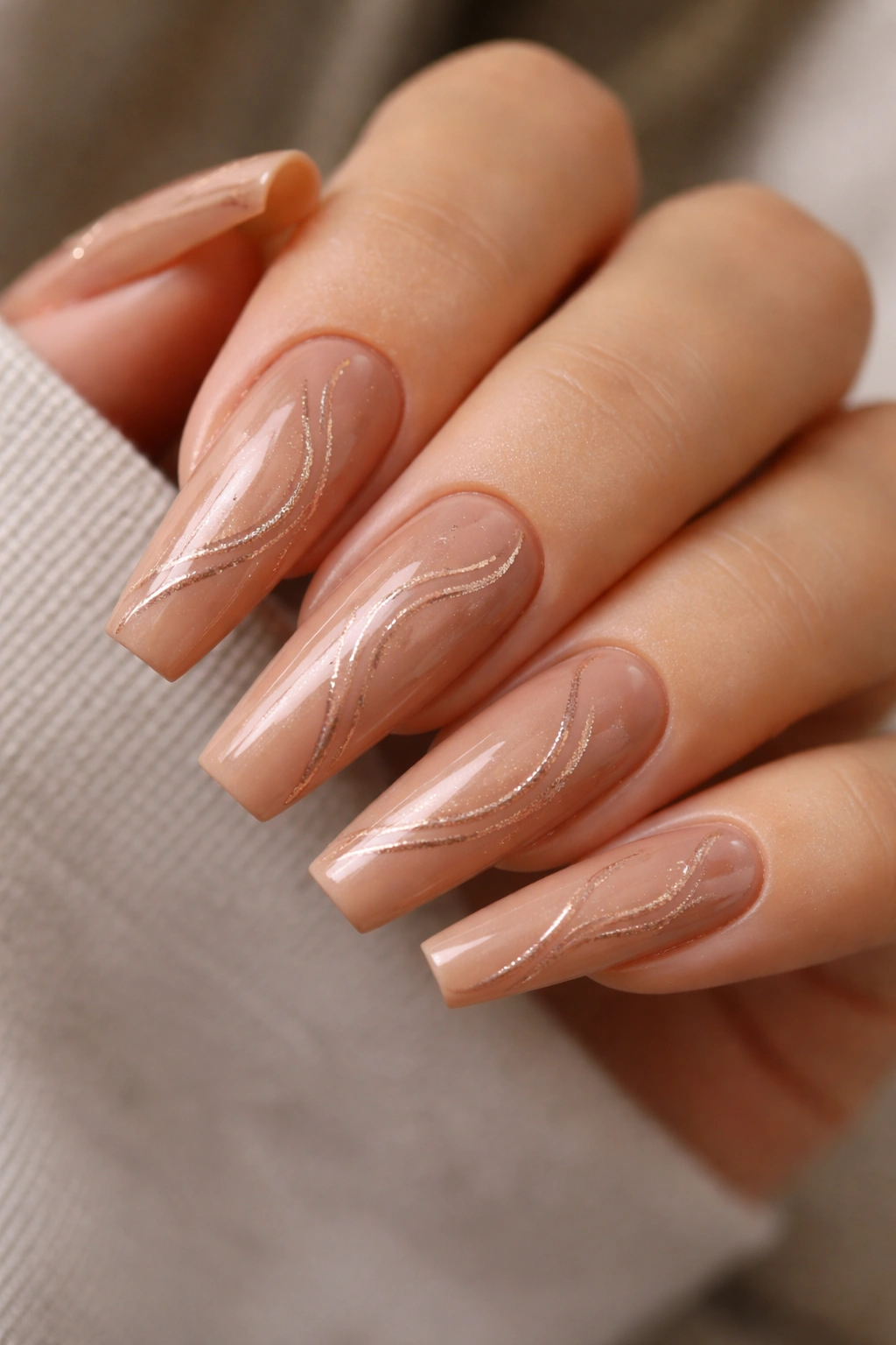 Close-up of coffin nails in peachy brown with rose gold swirls.