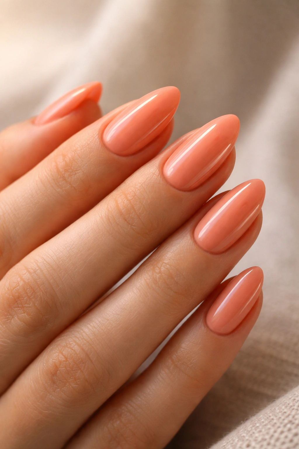 Close-up of peachy coral almond nails with semi-sheer finish