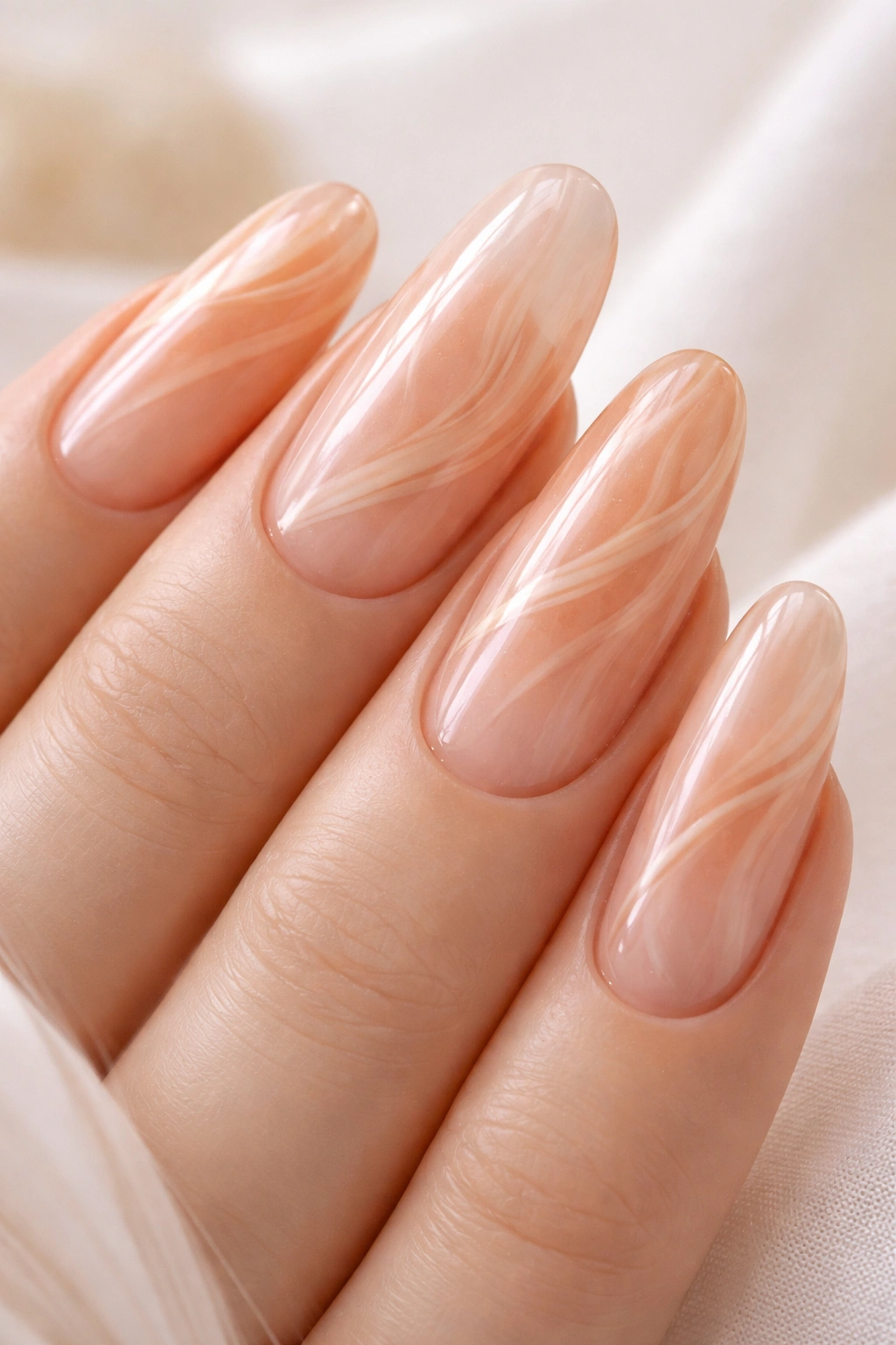 Close-up of peachy glass nails with subtle swirl patterns on long oval shapes