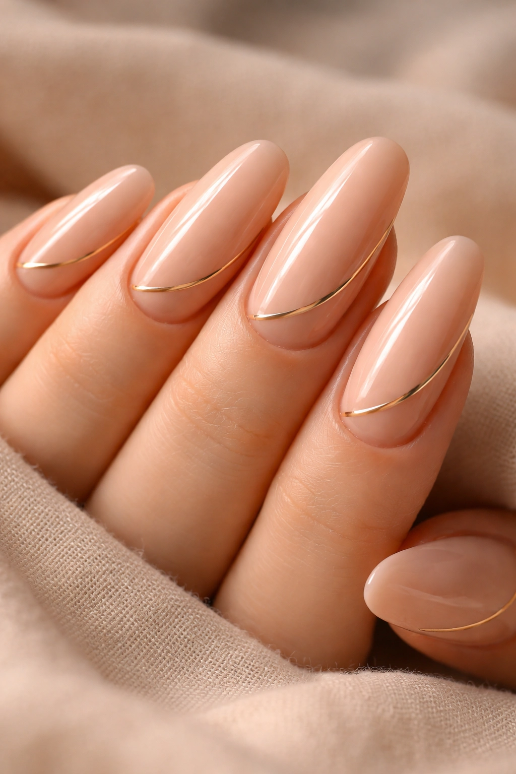 Close-up of peachy nude nails with thin gold stripes on long round nails