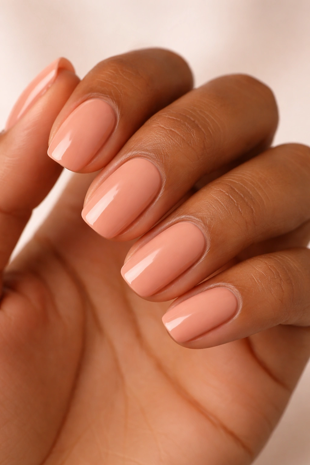 Close-up of nails painted peachy nude on warm-toned skin