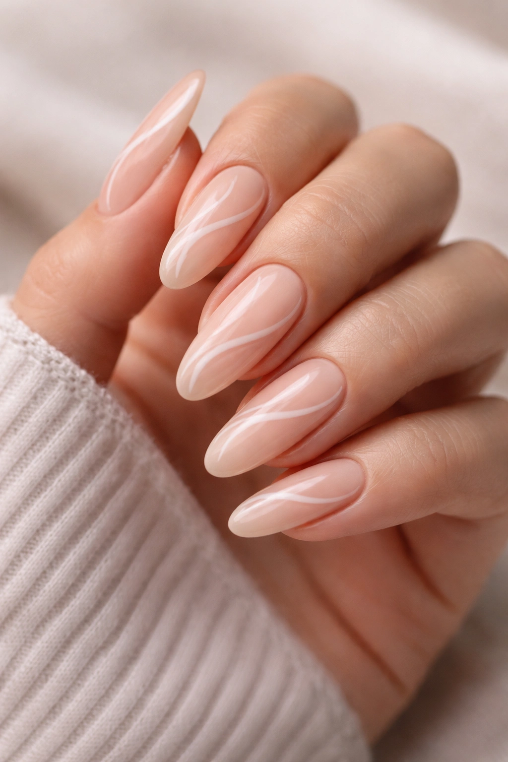 Close-up of peachy nude tapered oval nails with delicate white swirls