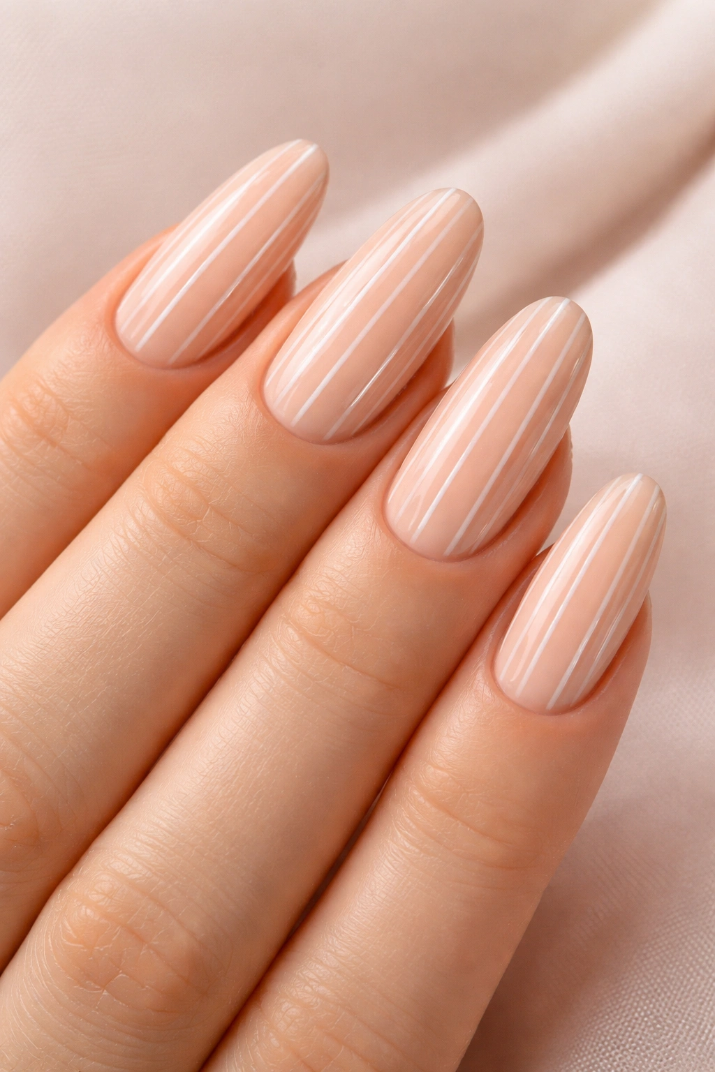 Peachy nude oval nails with thin white stripes.