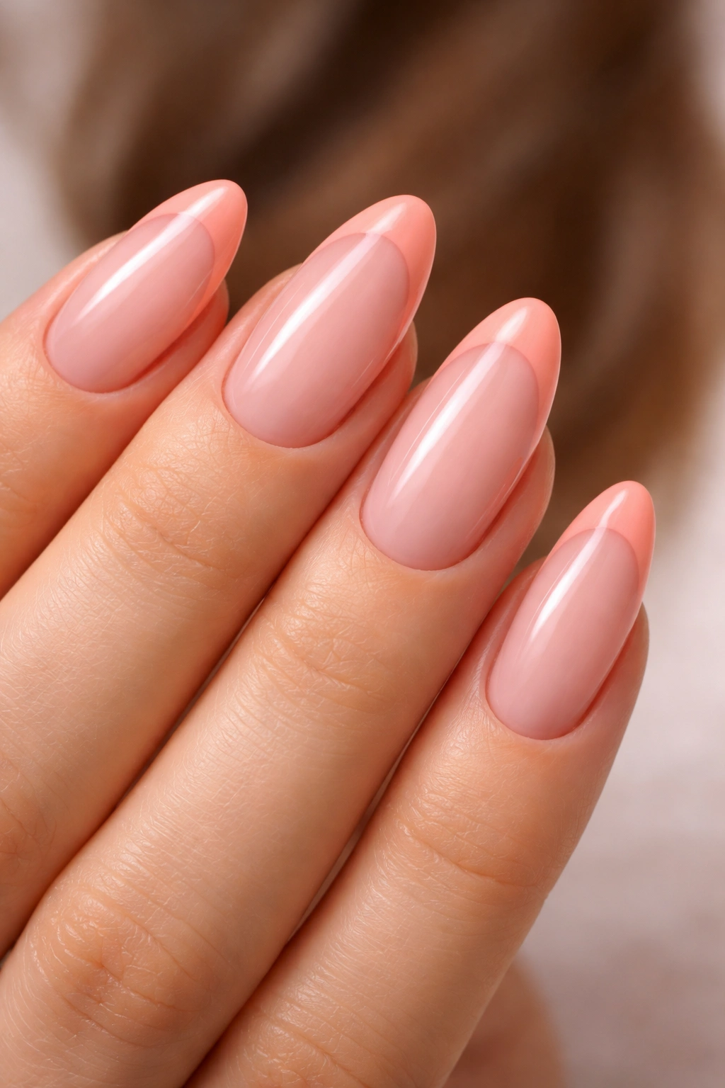 Almond nails with peachy pink French tips on a warm-toned background.