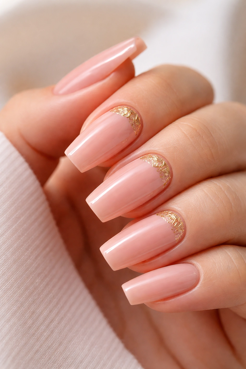 Close-up of peachy pink ballerina nails with irregular gold foil near the cuticle on accent nails, glossy finish