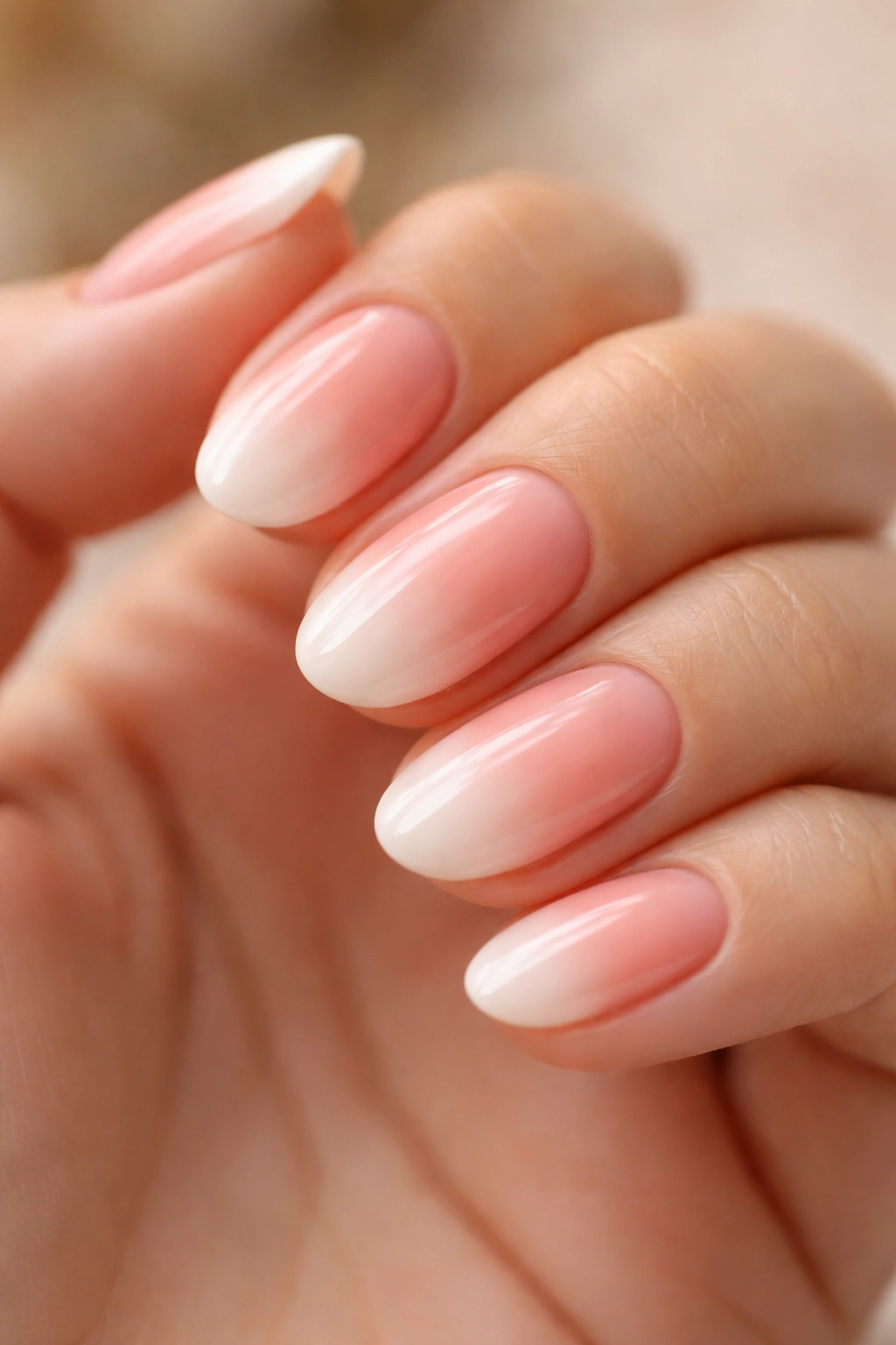 Close-up of short oval nails with peachy pink ombre and soft white blur