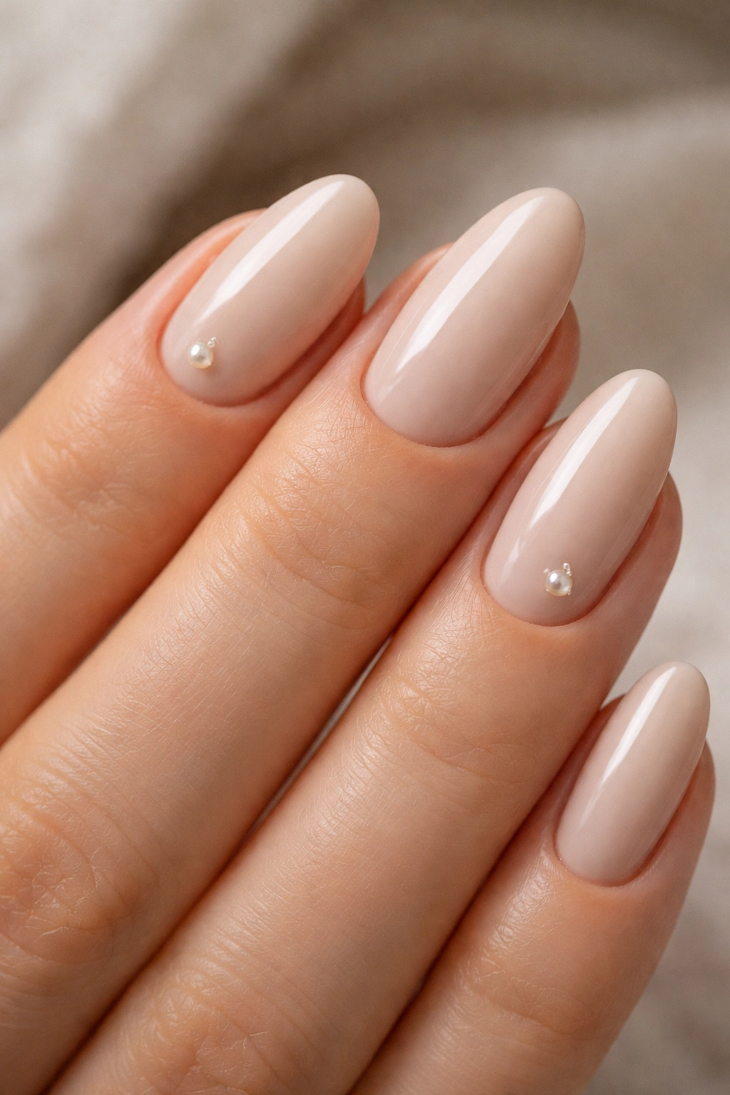 Close-up of beige almond nails with tiny pearl accents