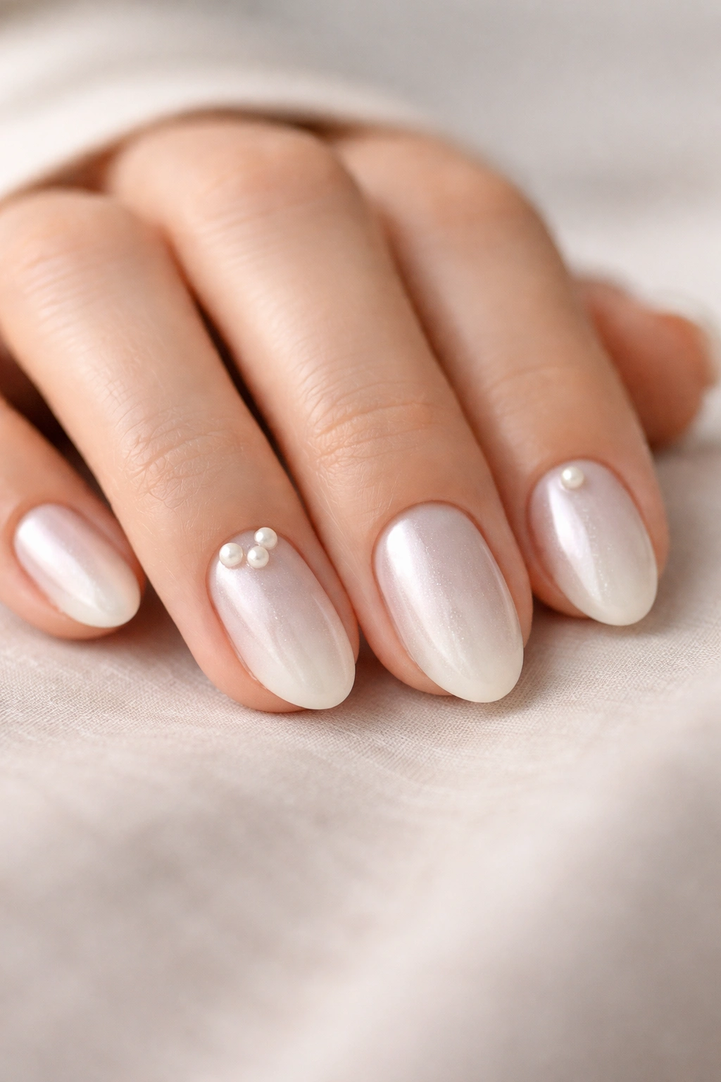 Close-up of short almond nails with balanced pearl accents on a tidy hand.