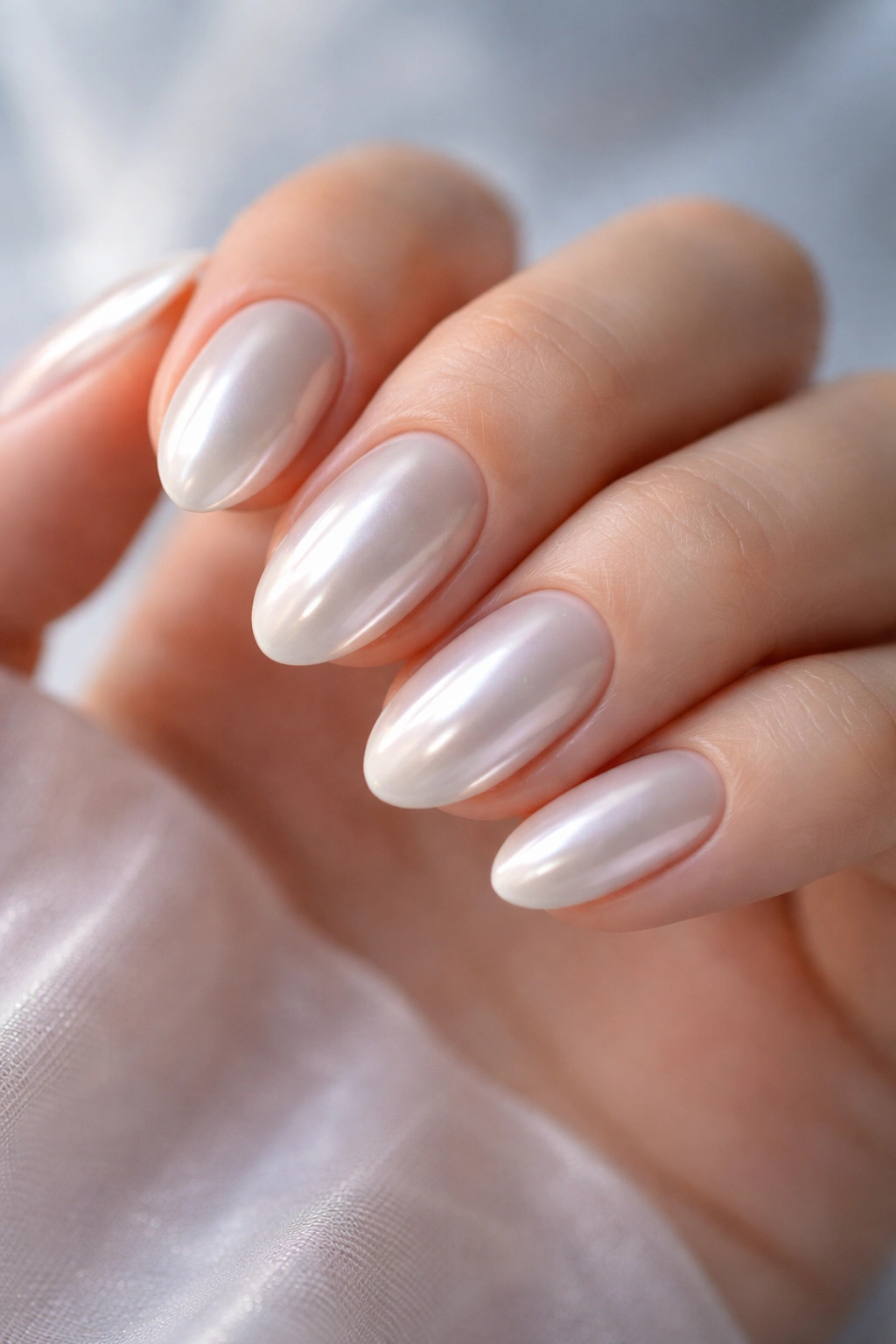 Close-up of short almond nails with pearl chrome finish reflecting soft light