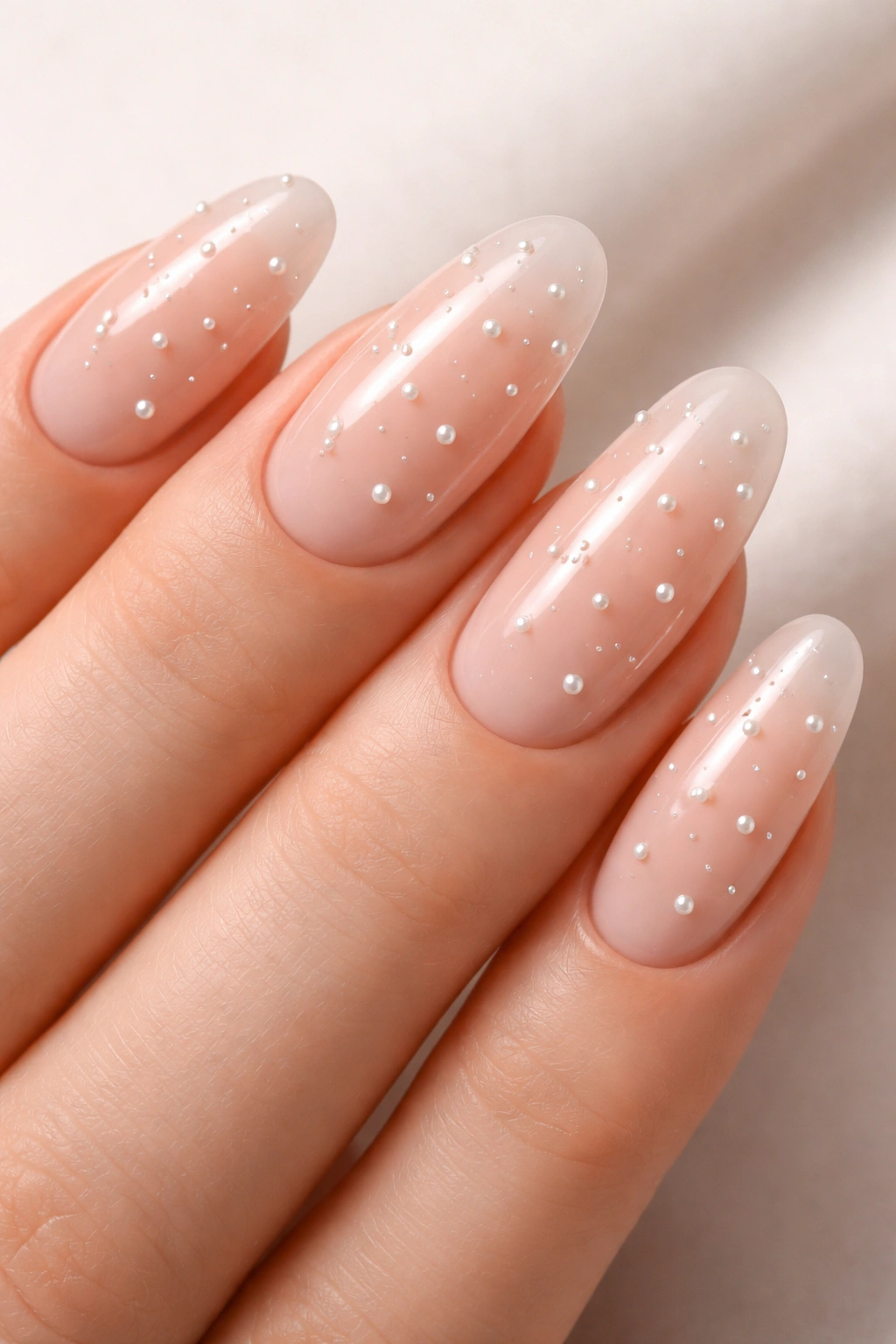 Close-up of long round acrylic nails with tiny pearl dot accents on nude base