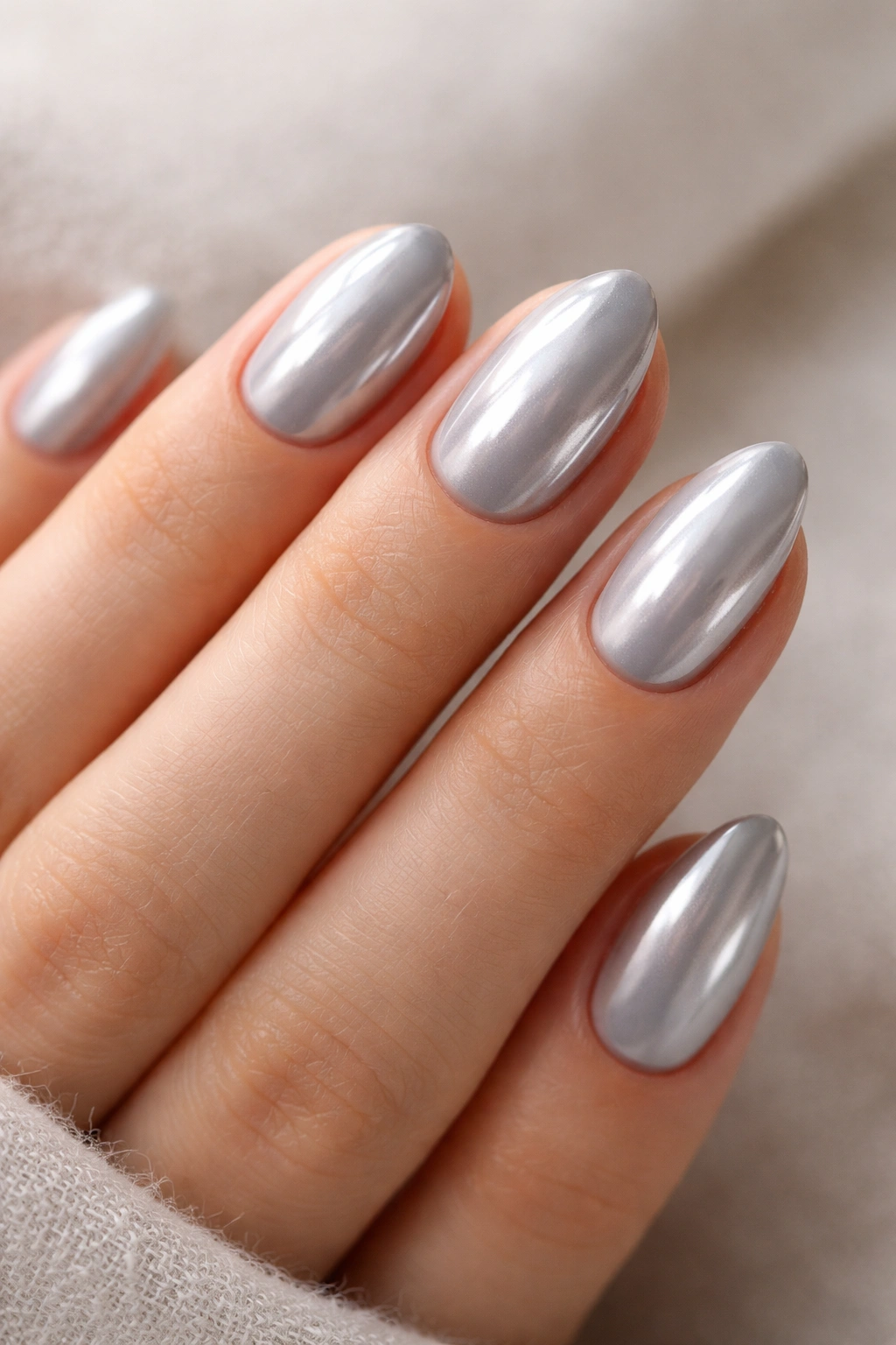 Close-up of short almond nails with pearl grey polish and chrome shine