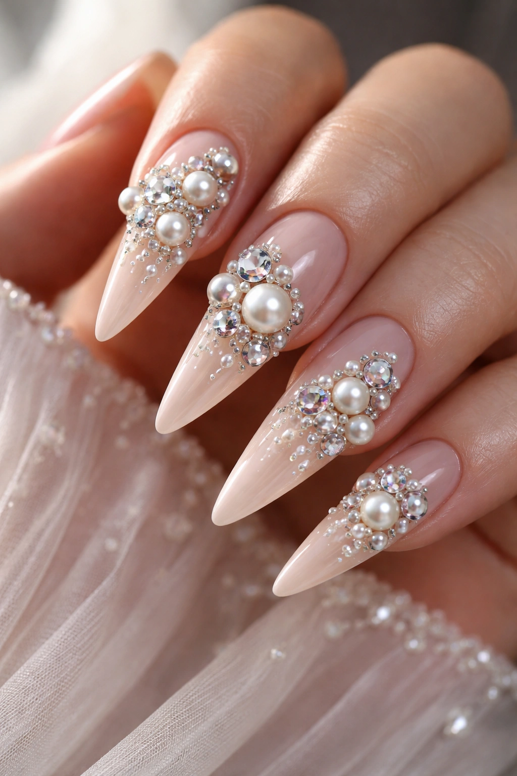 Close-up of stiletto nails with pearl and rhinestone clusters on a blush base.