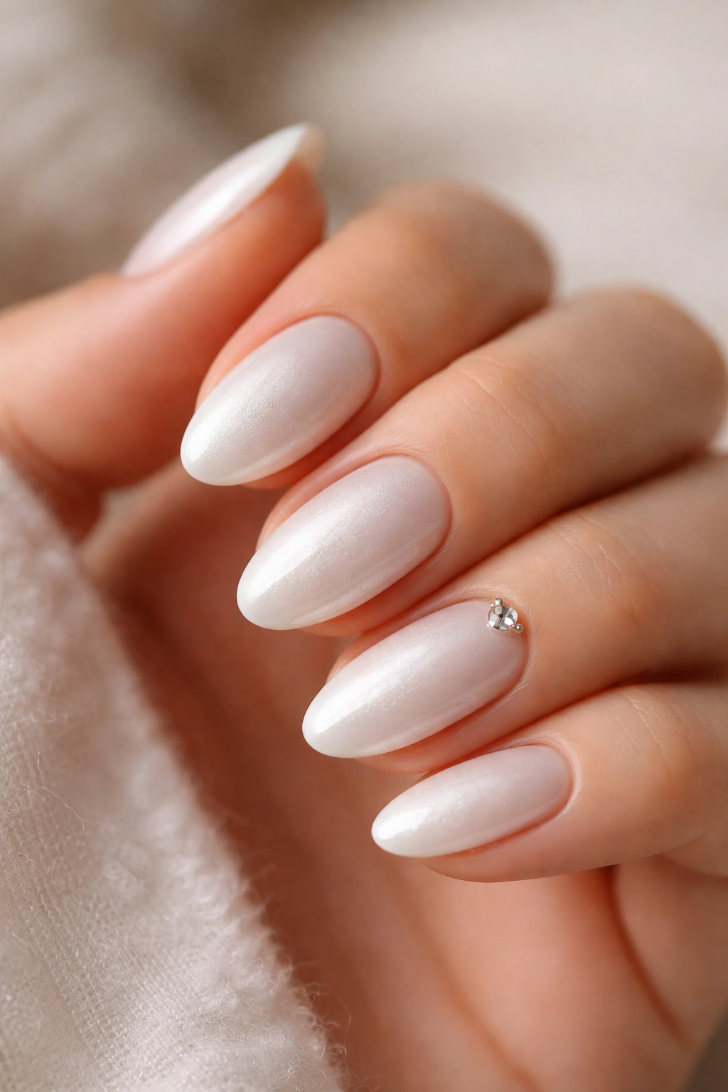Close-up of pearl white short almond nails with a small crystal on the accent nail.
