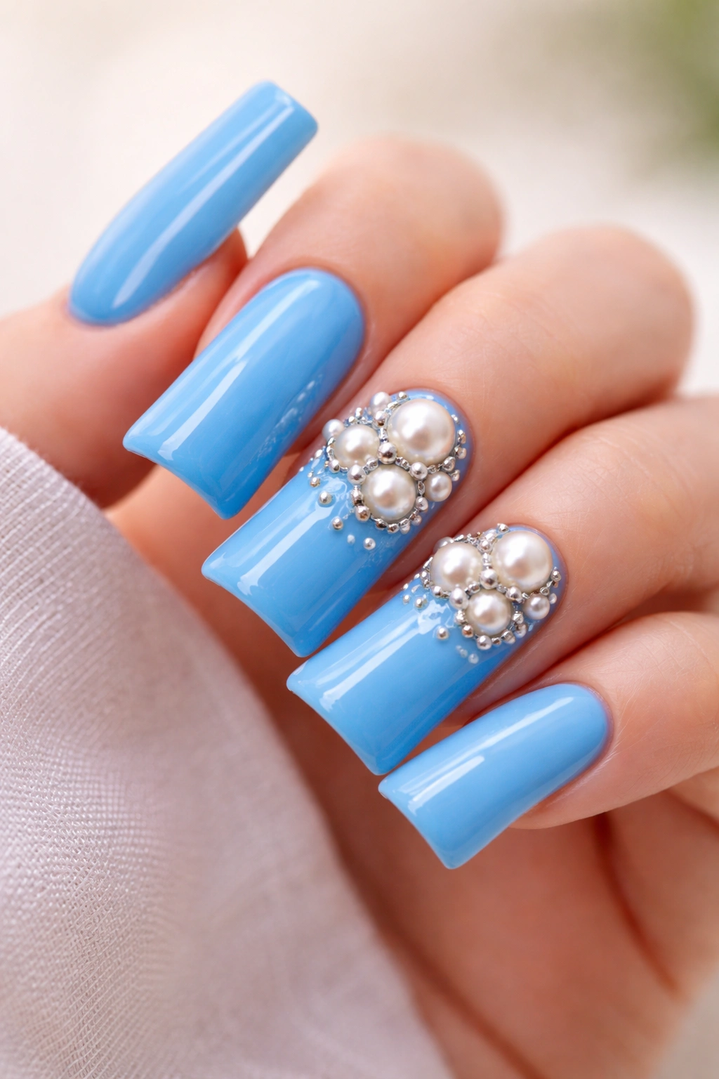 Close-up of glossy blue nails with pearl charms on a neutral background