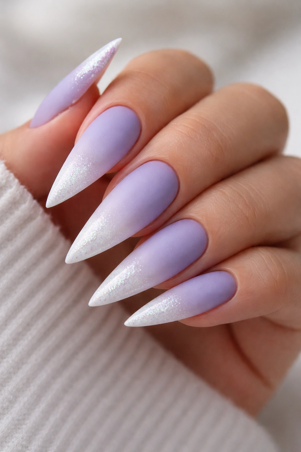 Close-up of stiletto nail with periwinkle to white ombre, matte finish, and shimmering tip.
