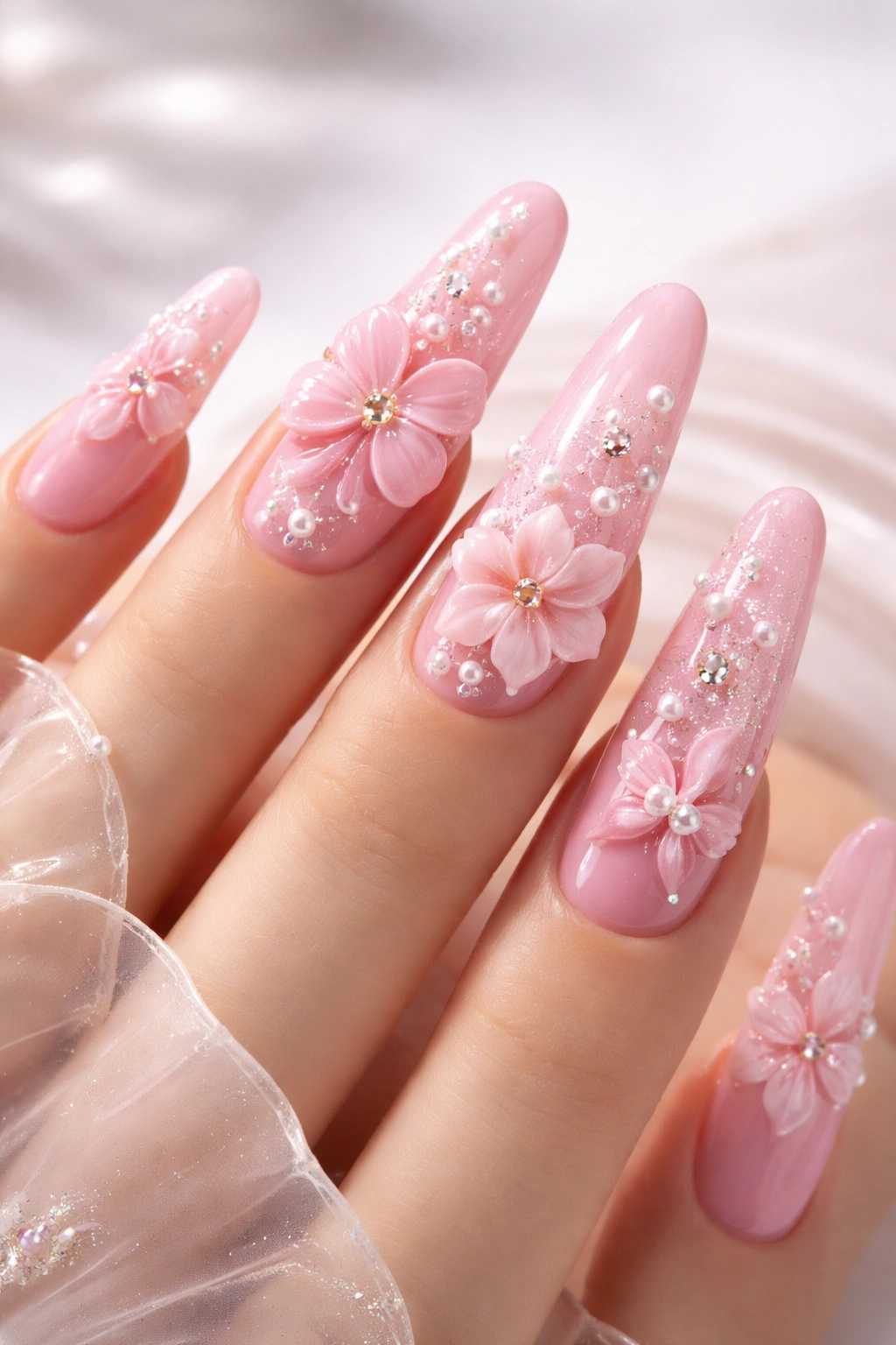 Close-up of pink nails with 3D embellishments like flowers on long almond nails