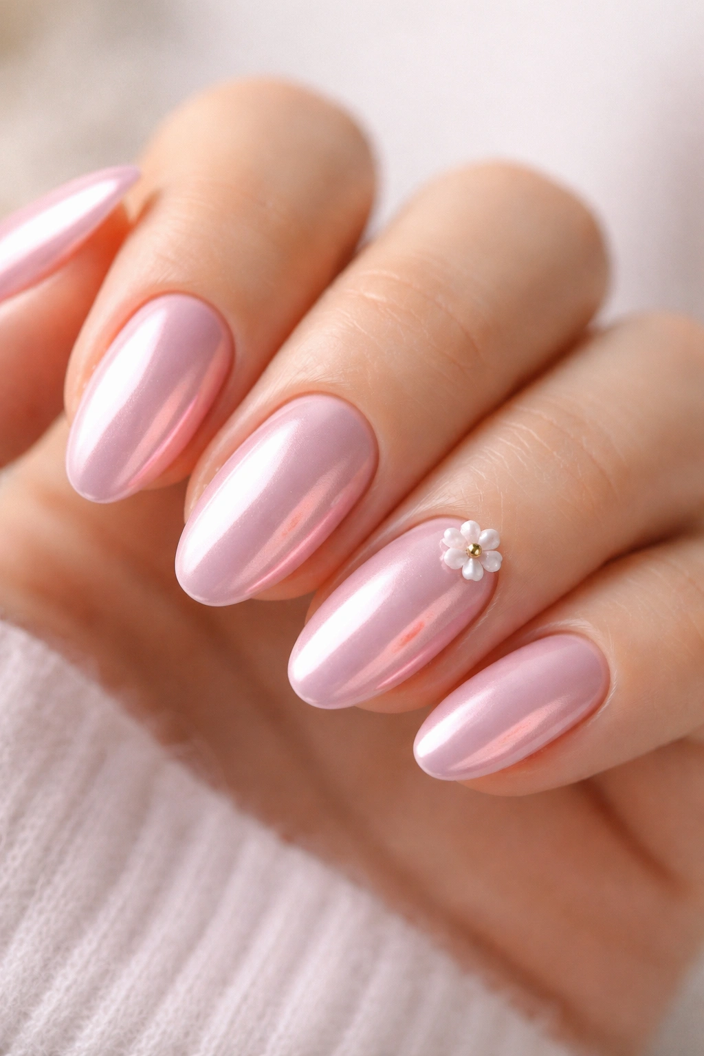Close-up of baby pink chrome nails with a tiny raised 3D flower accent
