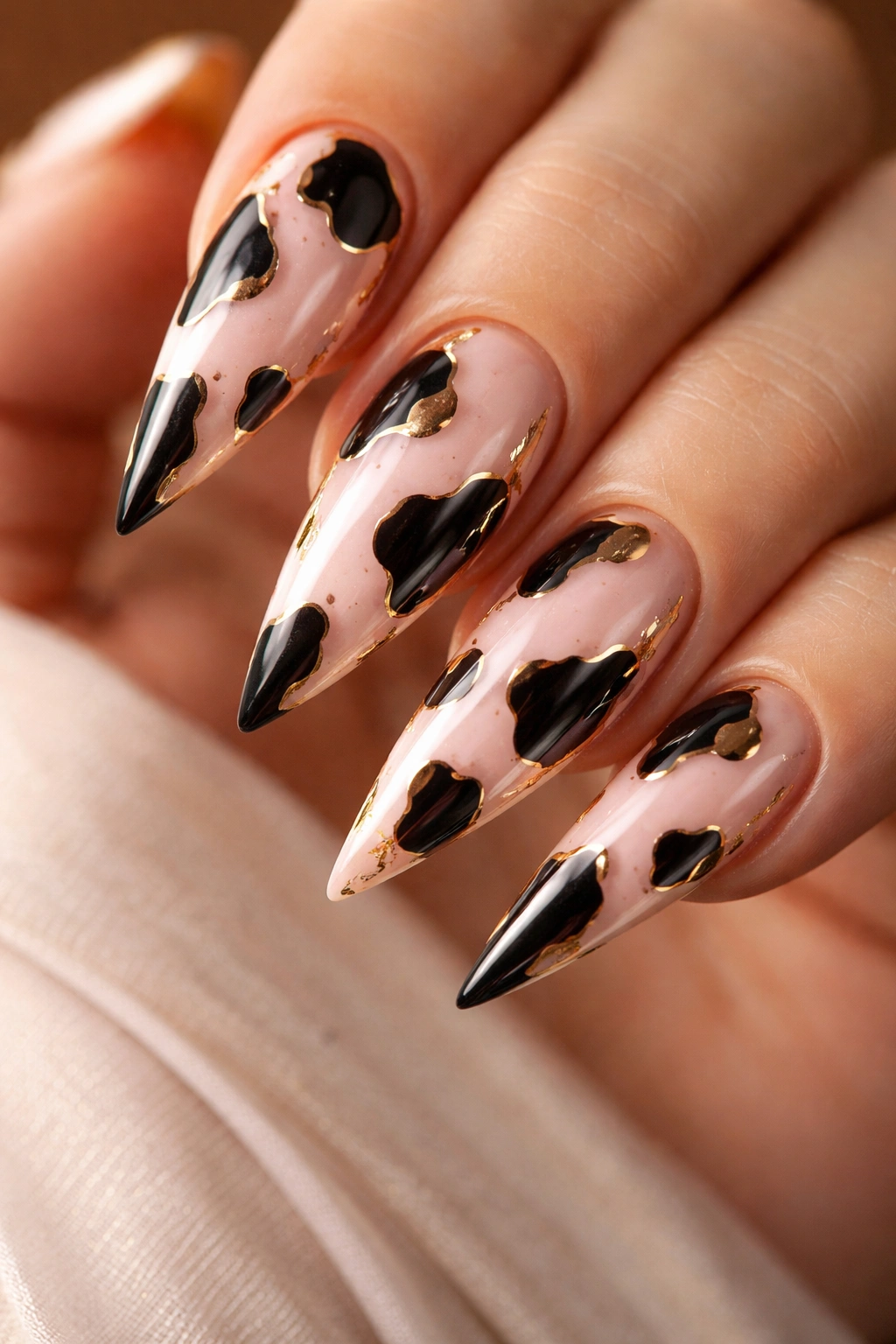 Close-up of glazed pink cow print stiletto nails with gold accents