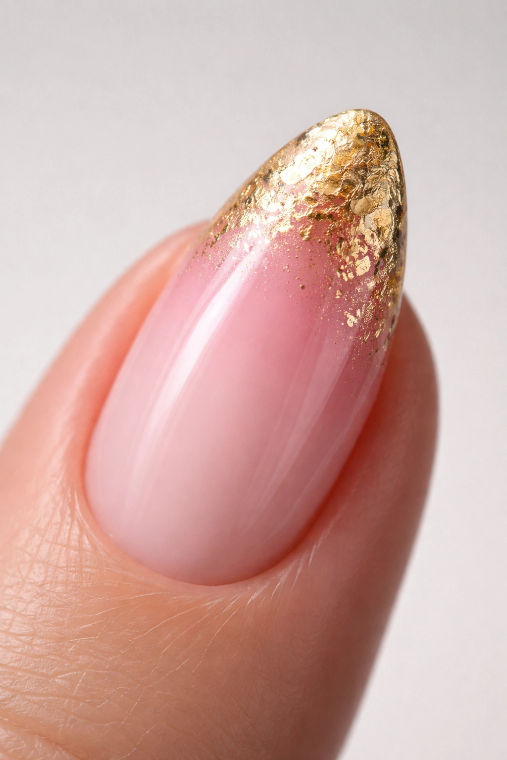 Close-up of an almond nail with pink ombre and gold foil tip texture