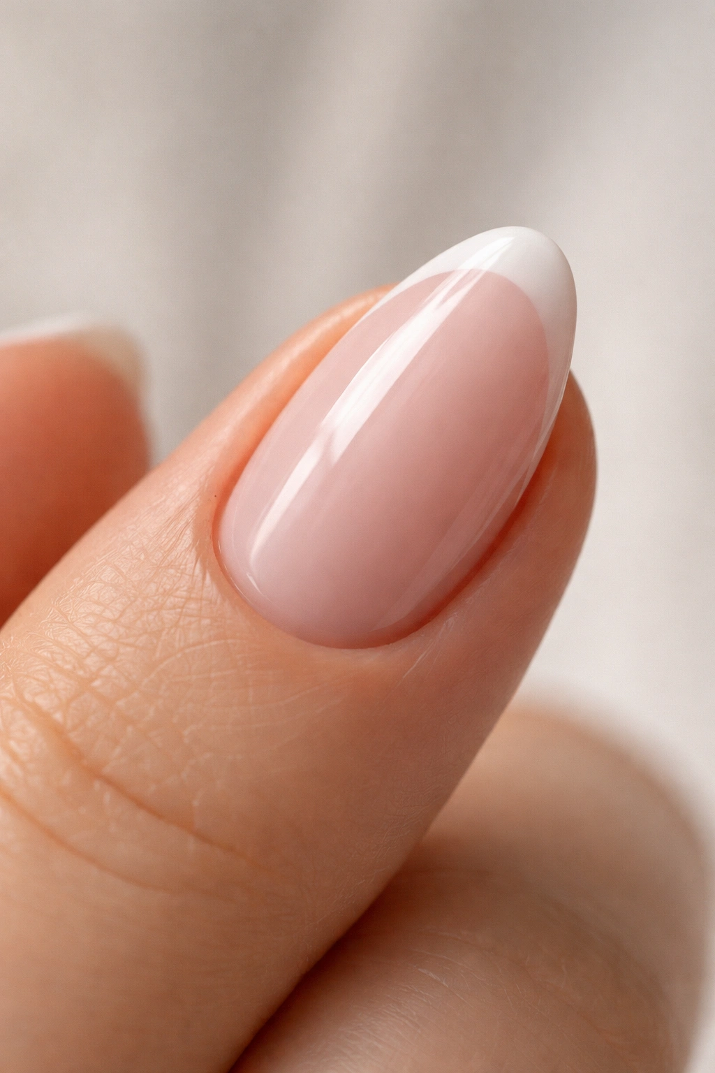 Close-up of pink French almond nail with sheer base and slim white tip in soft studio lighting
