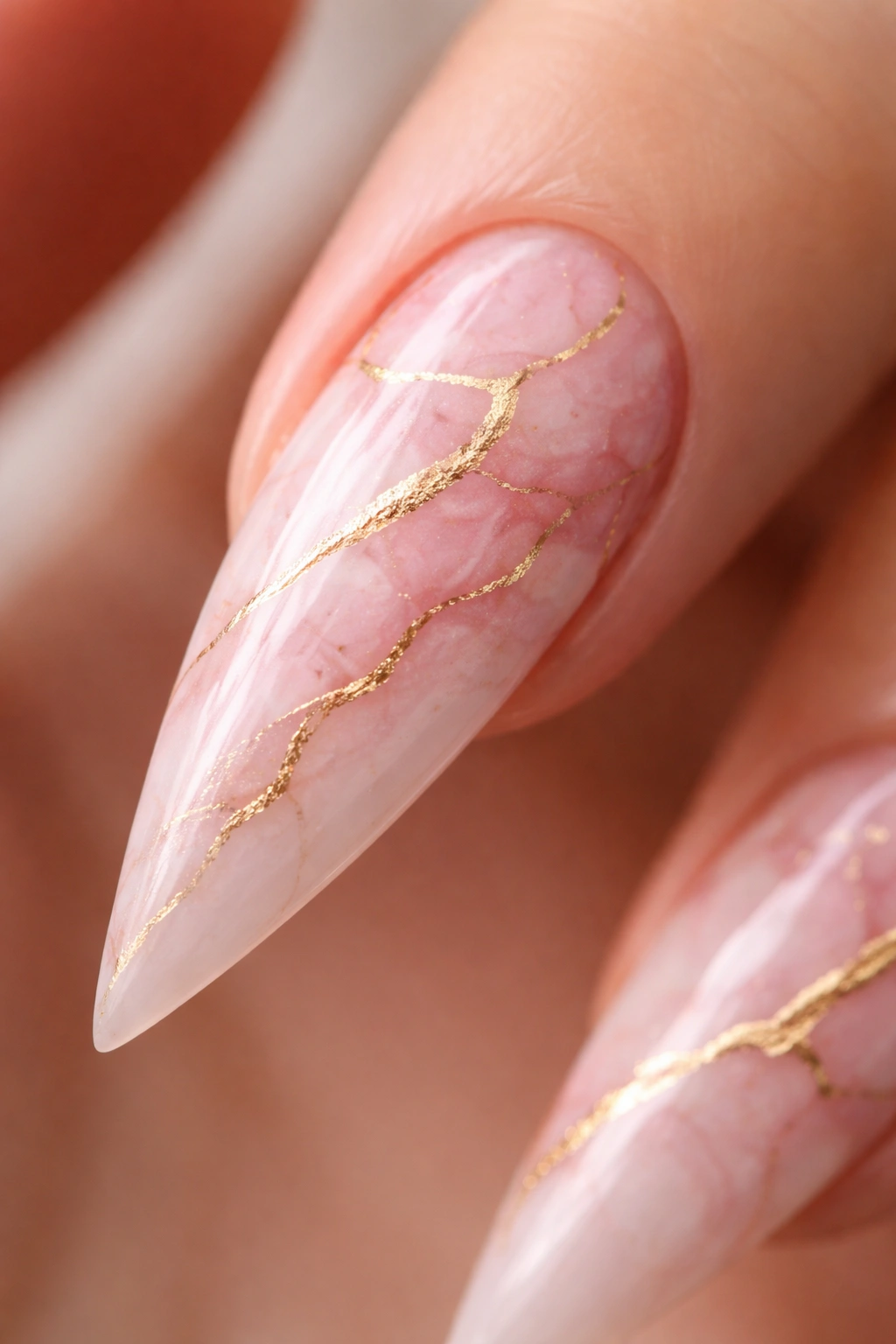 Close-up of a pink marble stiletto nail with gold veining