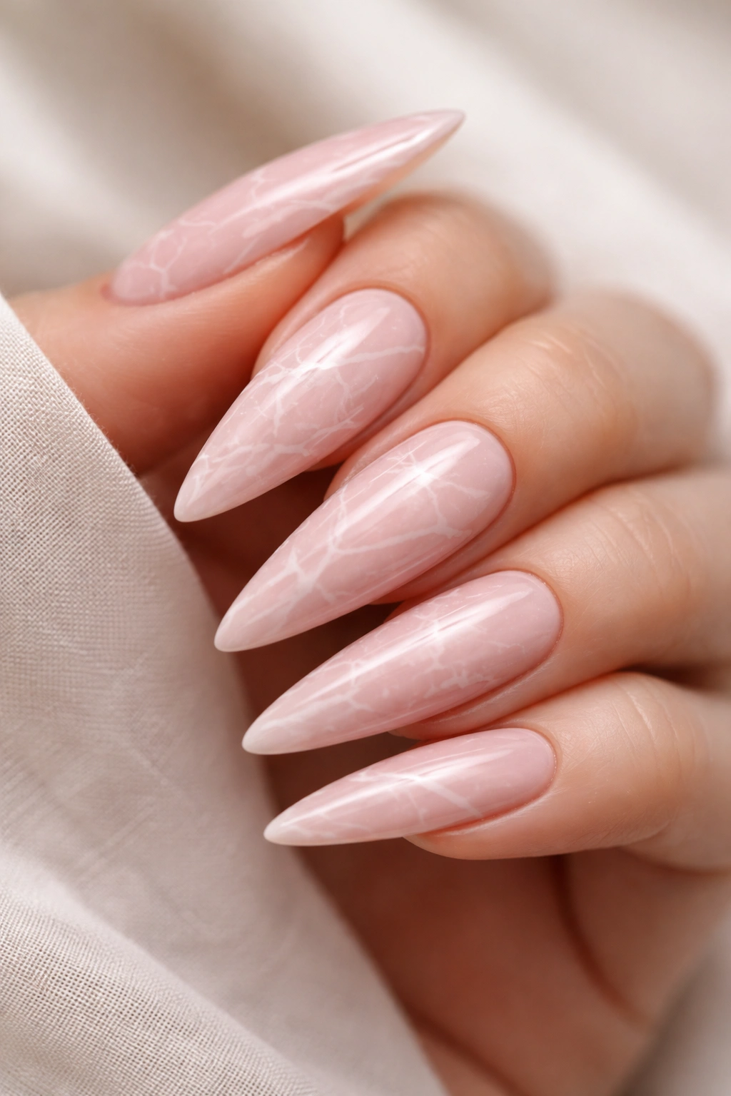 Close-up blush pink stiletto nails with white marble veining.