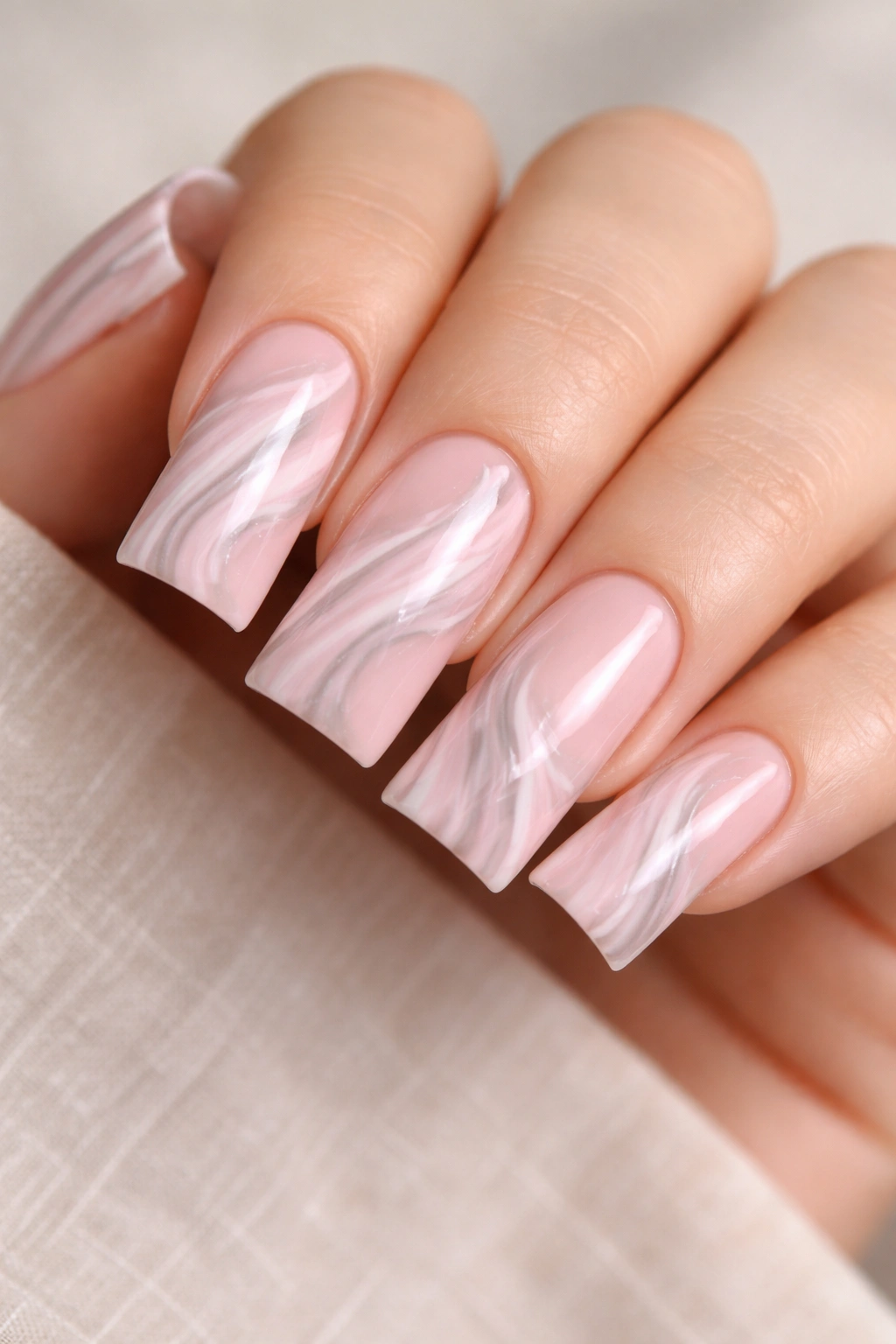 Close-up of nails with soft pink marble design featuring white and gray swirls along the duck nail curve