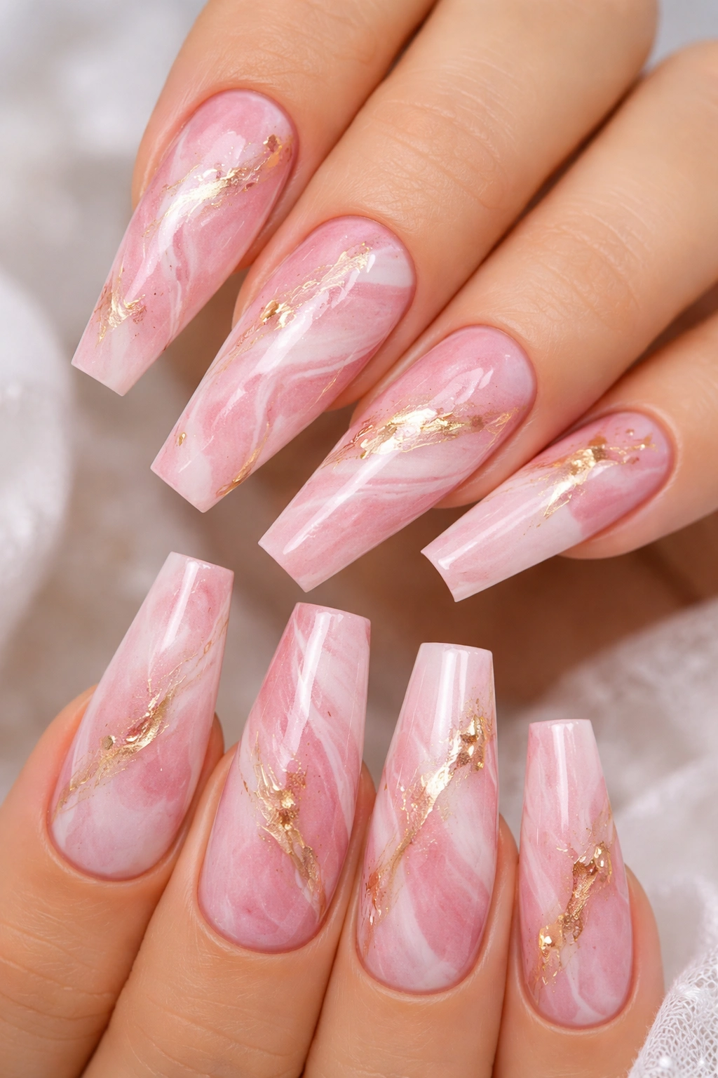 Close-up pink marble nails with white swirls and gold foil