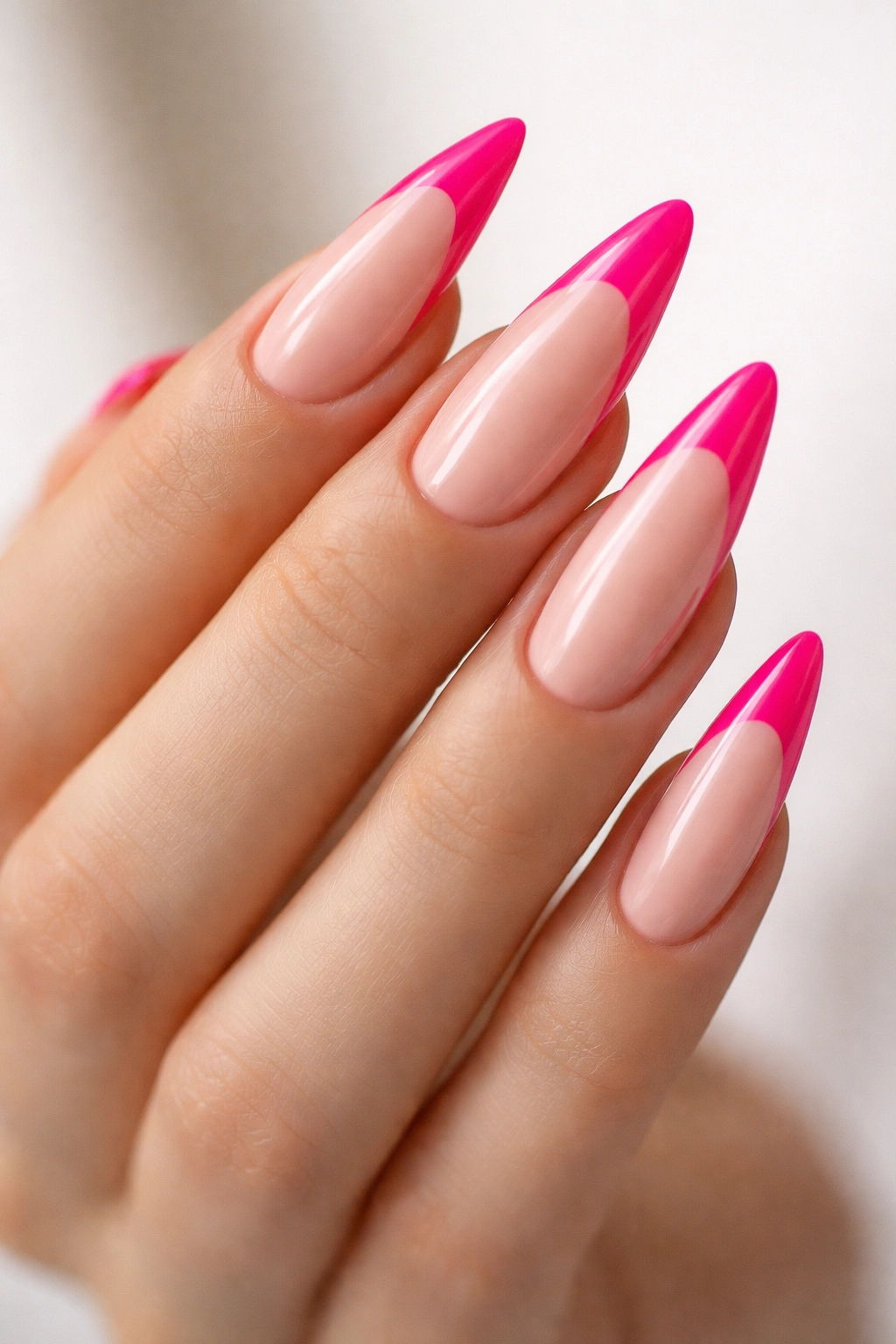 Close-up of long almond nails with hot pink tips and glossy finish in a neutral studio