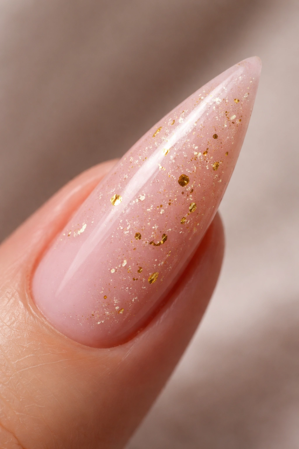 Close-up of a stiletto nail with pale pink base and gold foil flecks