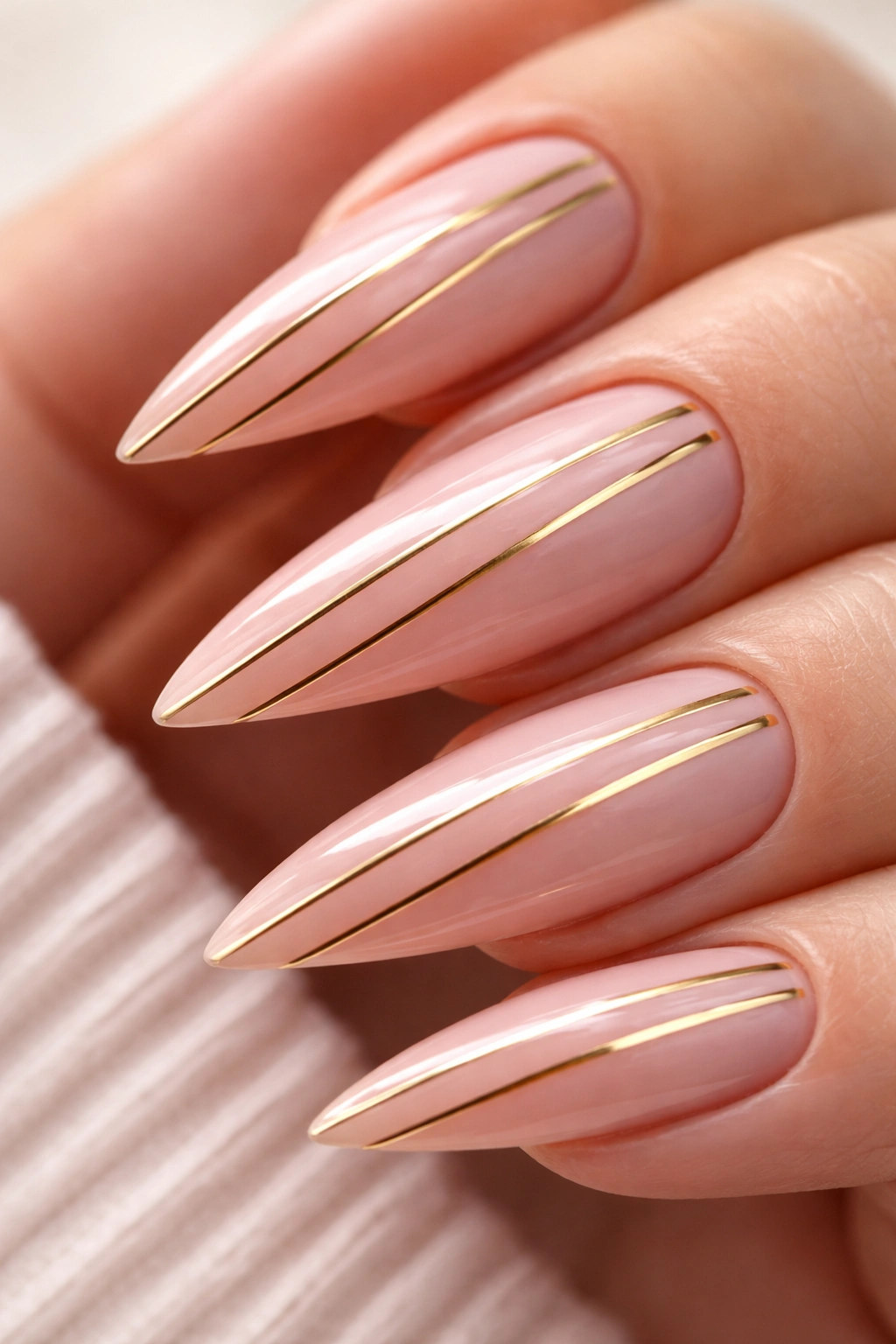Close-up of a stiletto nail with pink base and gold stripes