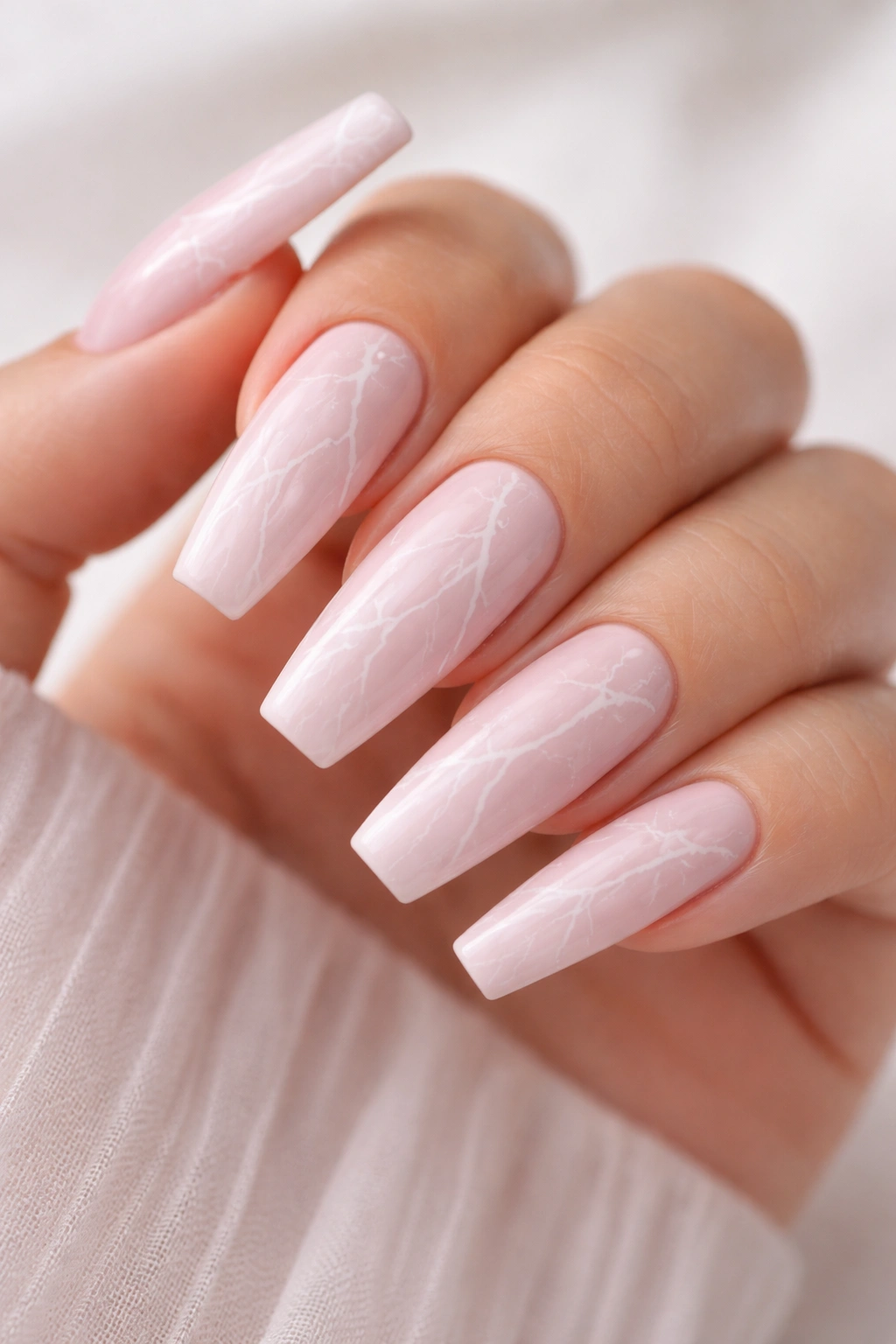 Close-up of soft pink coffin nails with white marble veining.