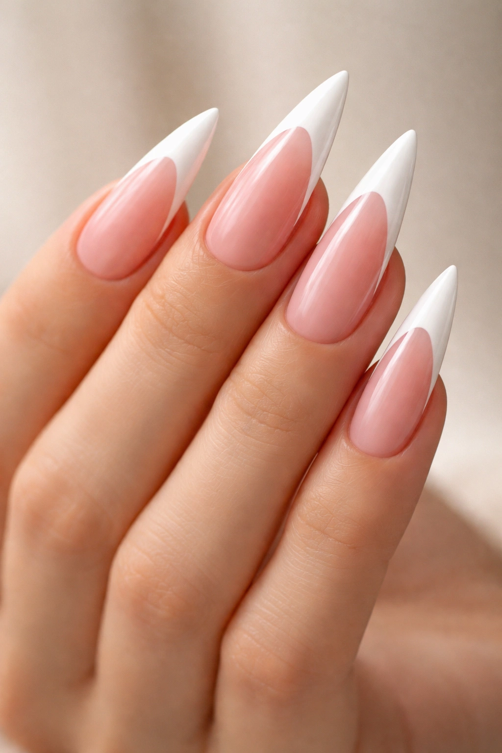 Close-up of a hand with classic pink and white French tip stilettos nails on a neutral backdrop