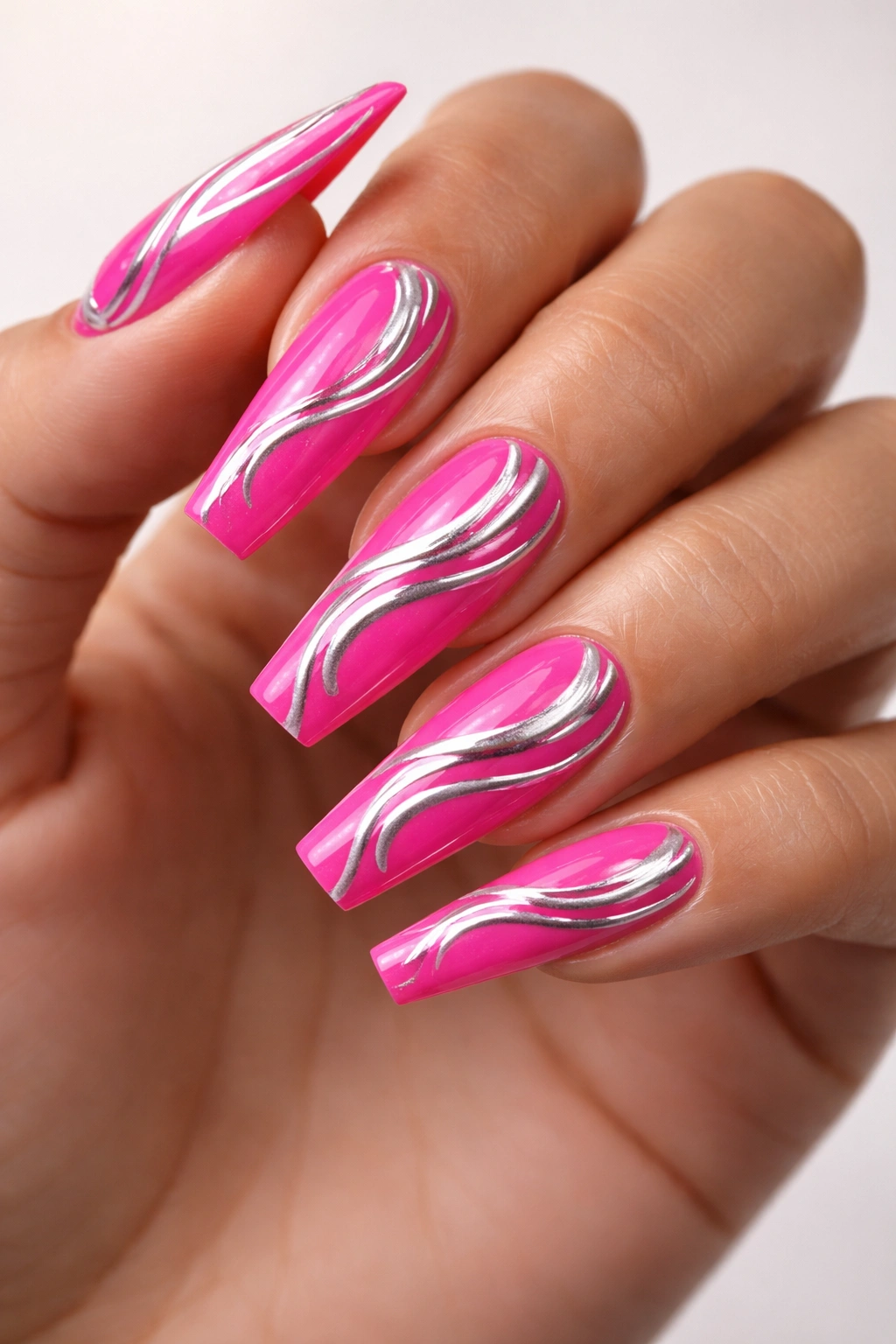 Close-up of coffin nail with hot pink base and silver swirl accents along the curve