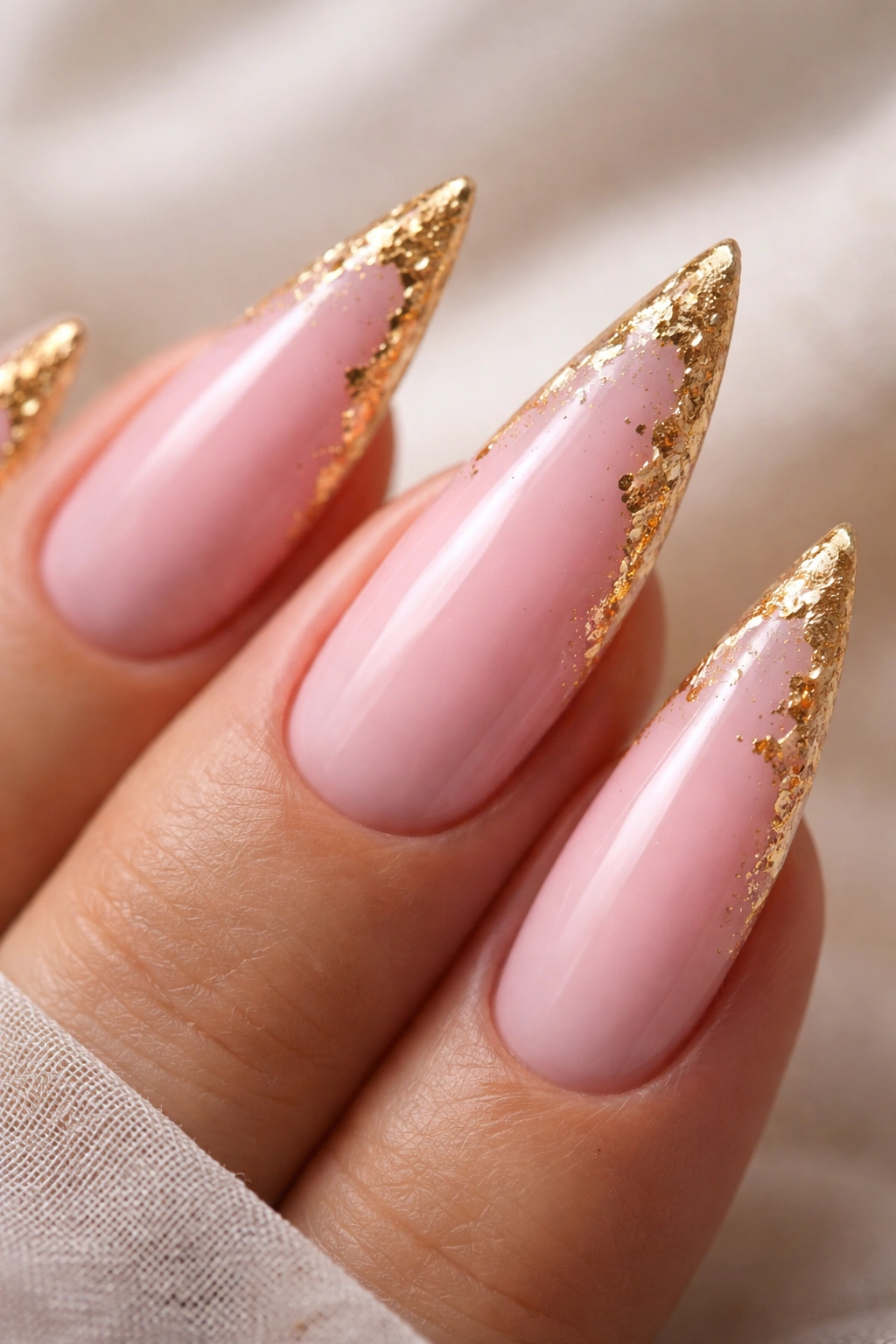Close-up of pink stiletto nail with gold leaf accents along the edge