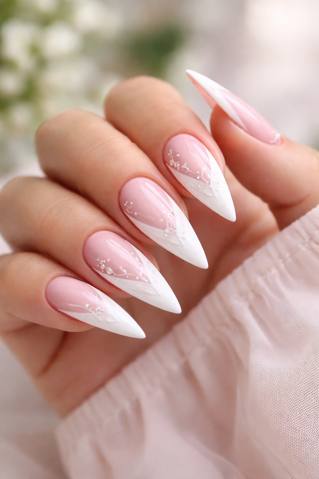 Close-up of pink stiletto nails with a white reverse French and decorative nail art.