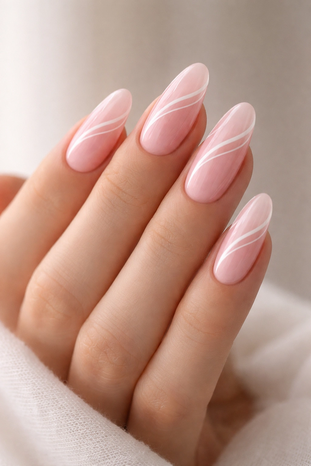 Close-up of long oval nails with pink base and white swirl art on a neutral background