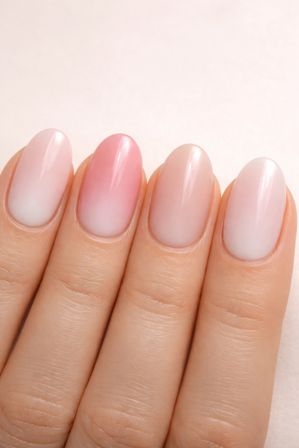 Close-up of four short oval nails with varied pink-to-white ombre on a clean background