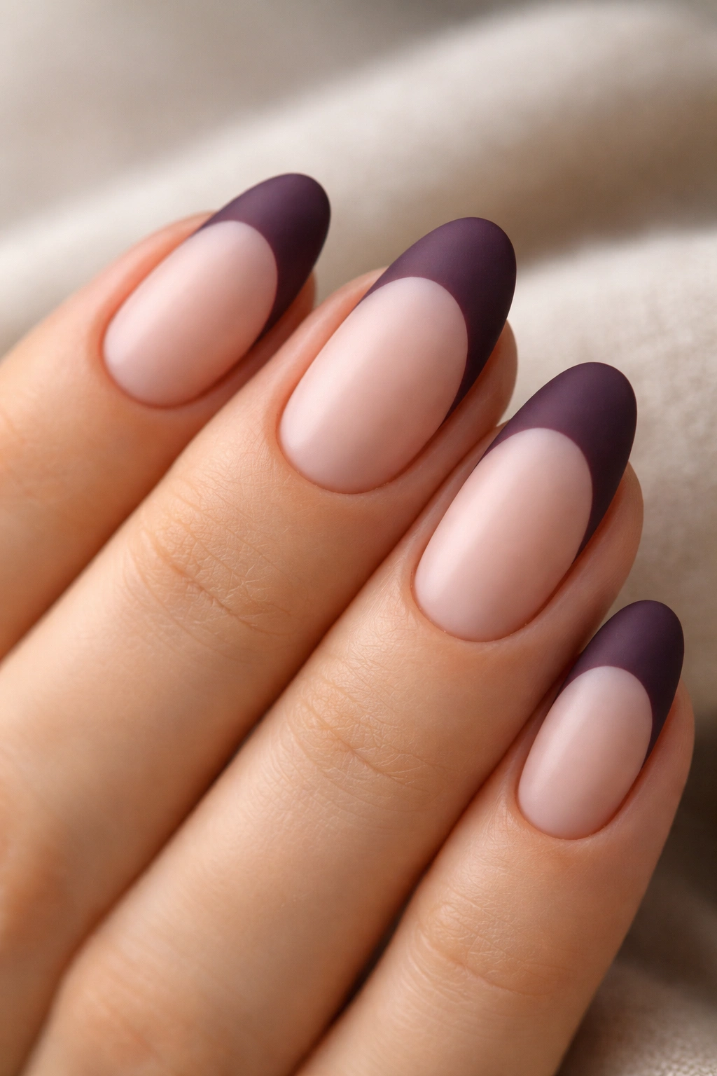 Close-up of a short almond nail with a matte deep plum tip on a nude base