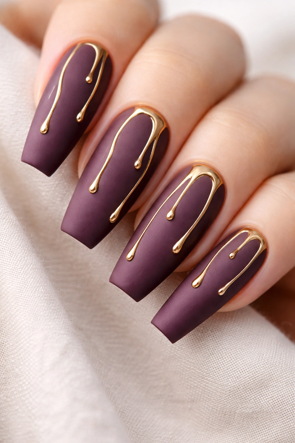 Close-up of matte plum coffin nails with a thin metallic gold drip