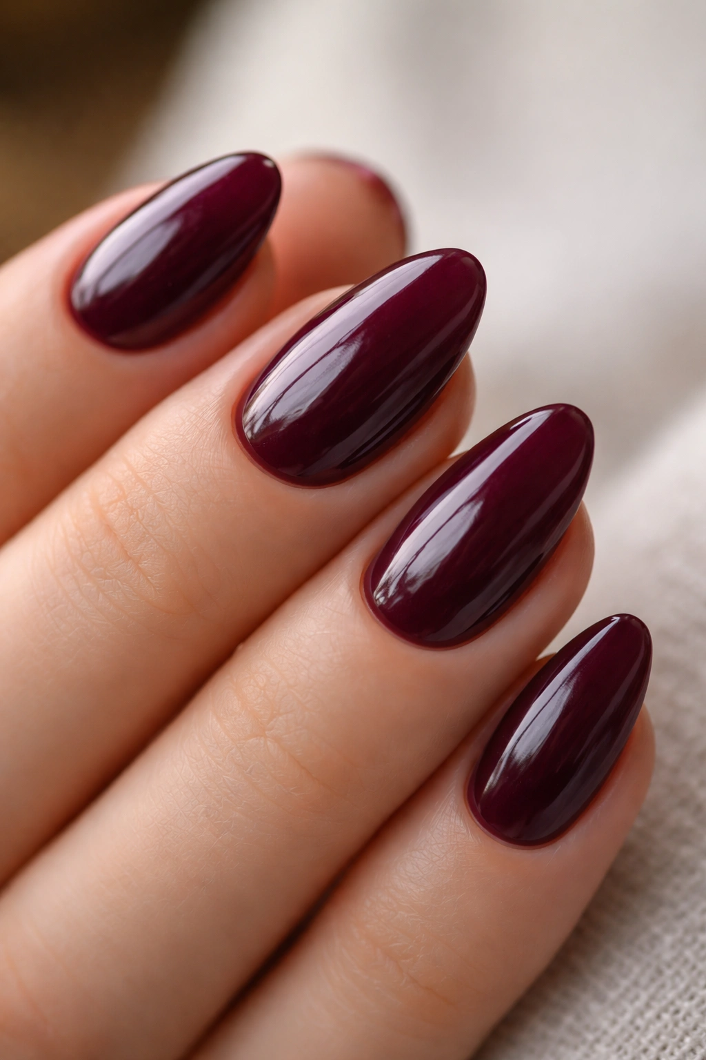 Close-up of a short almond nail in deep plum gloss with high shine