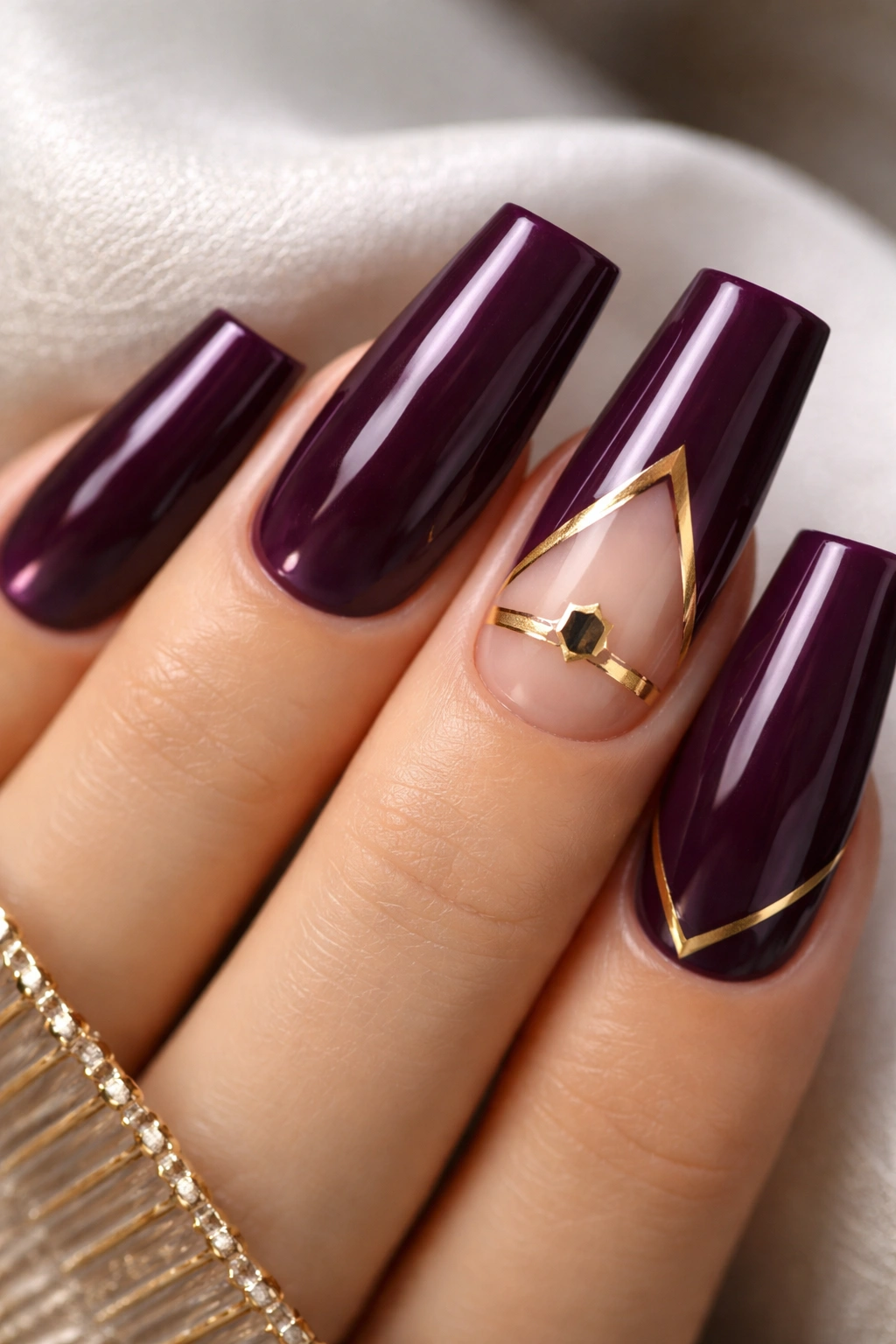 Close-up of deep plum nails with gold geometric accents on a couple nails