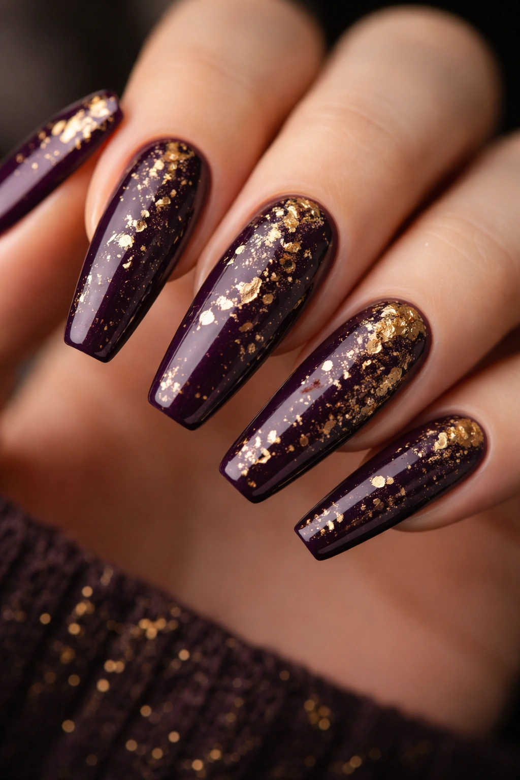 Close-up of deep plum coffin nails with gold metallic splatter