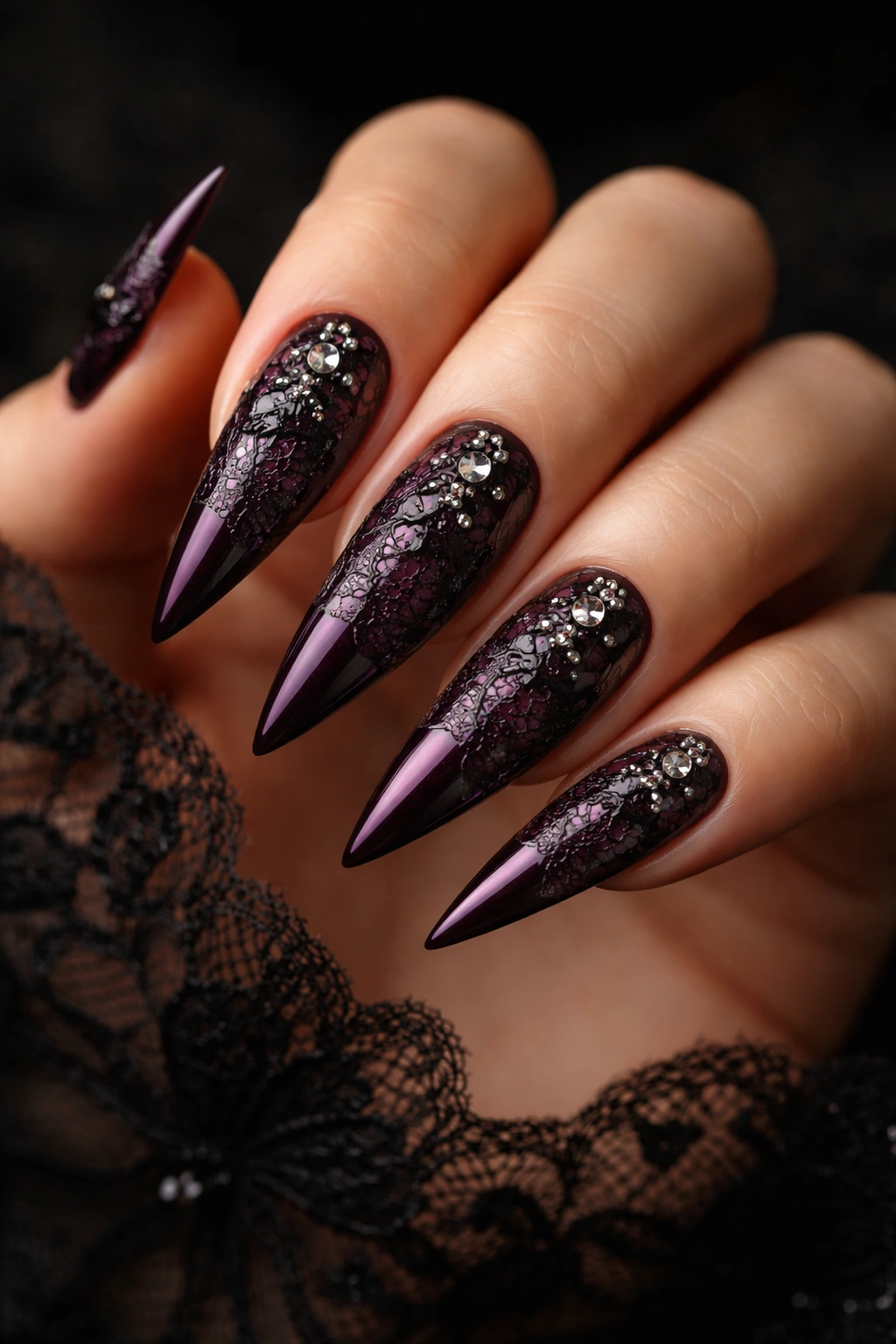 Close-up of deep plum stiletto nails with black lace and diamond accents