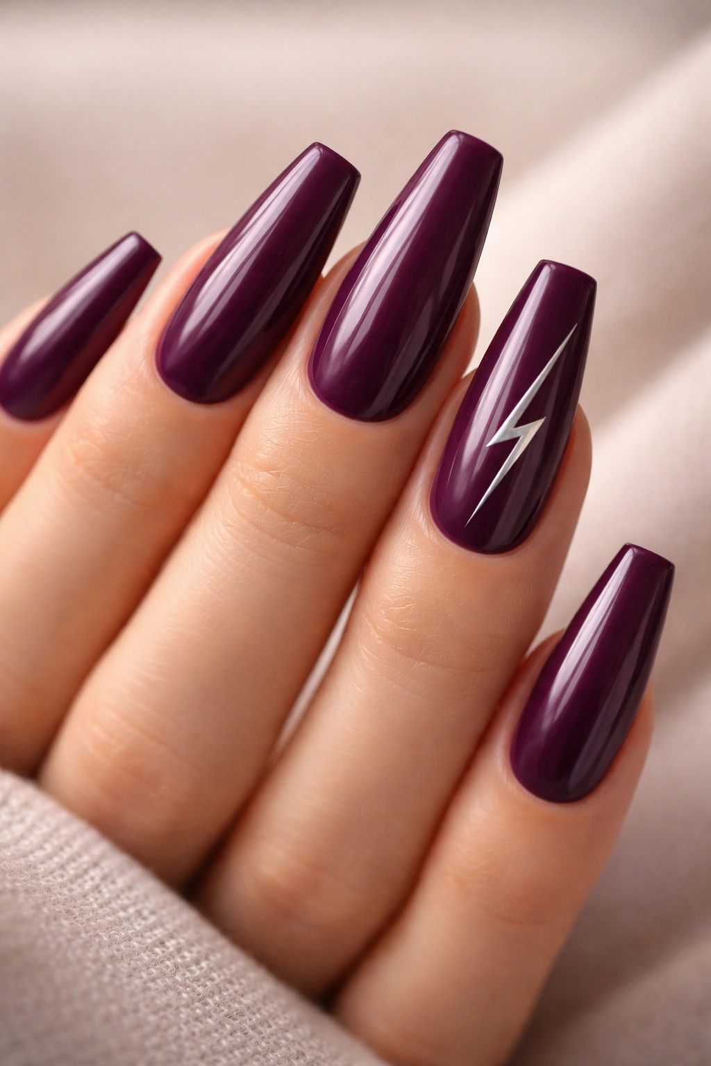 Close-up of coffin nails in rich plum with a thin silver lightning bolt accent