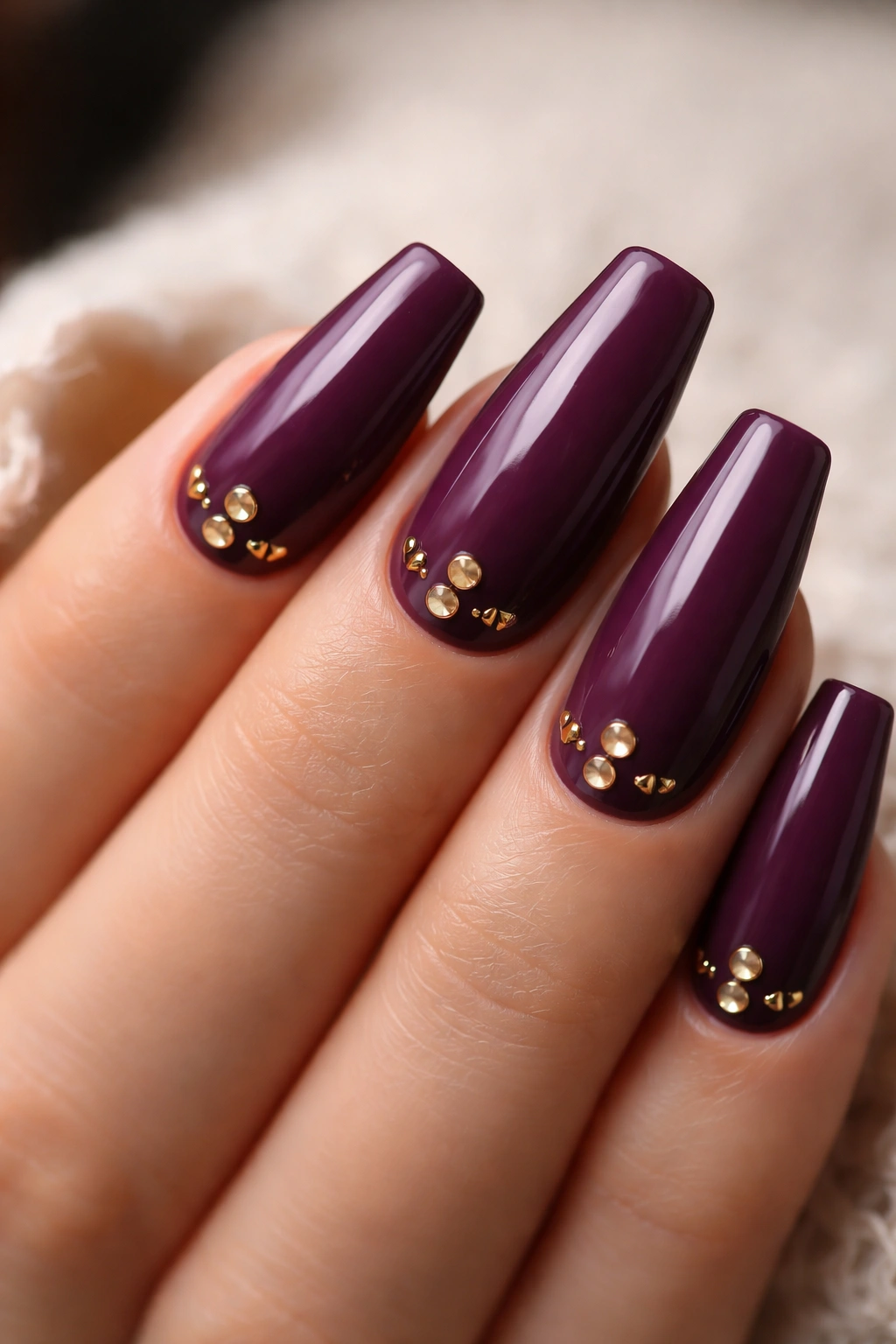 Deep plum nails with gold studs near cuticle in close-up